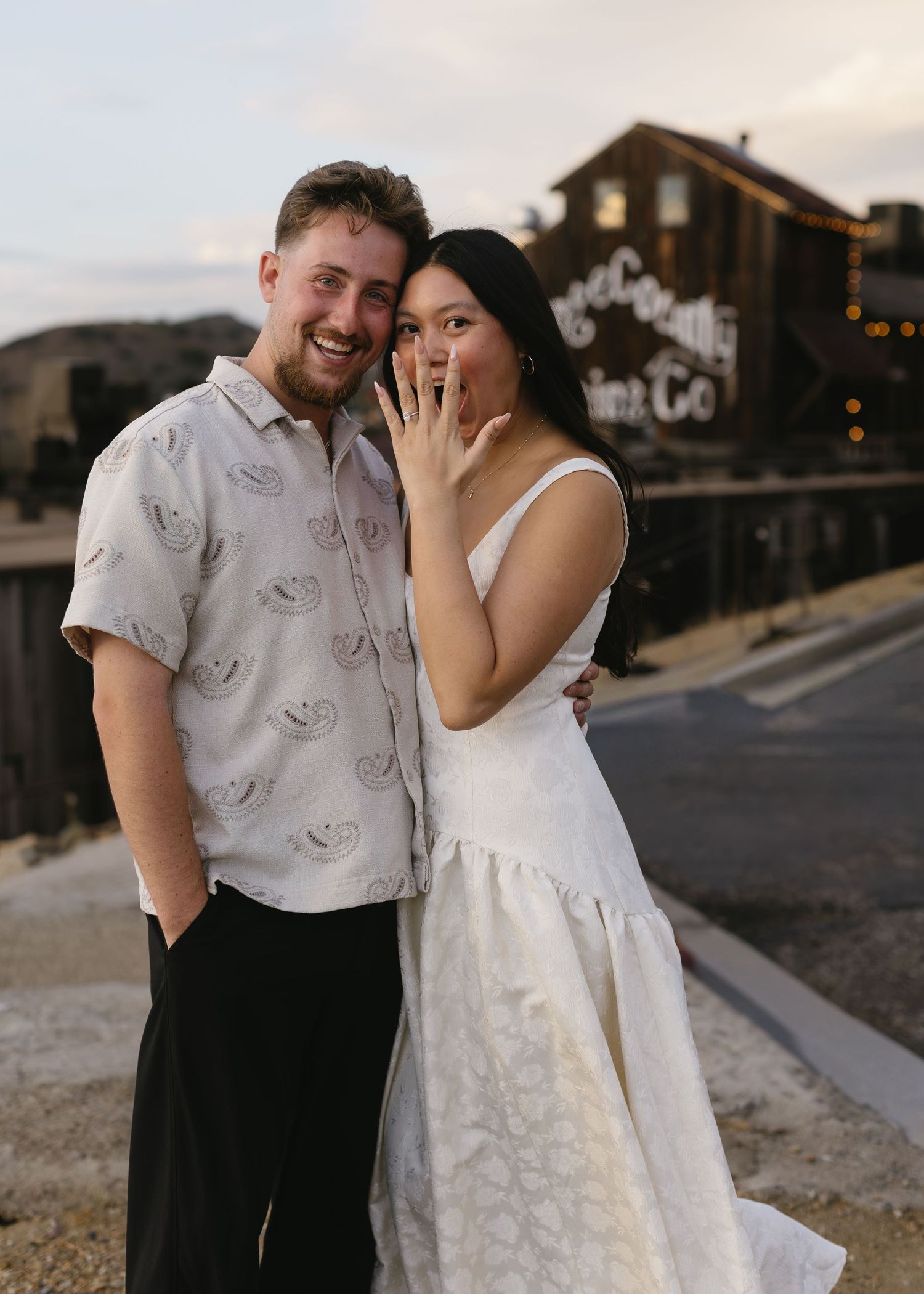 A couple in white clothing sharing romantic moments on a suburban street at dusk.