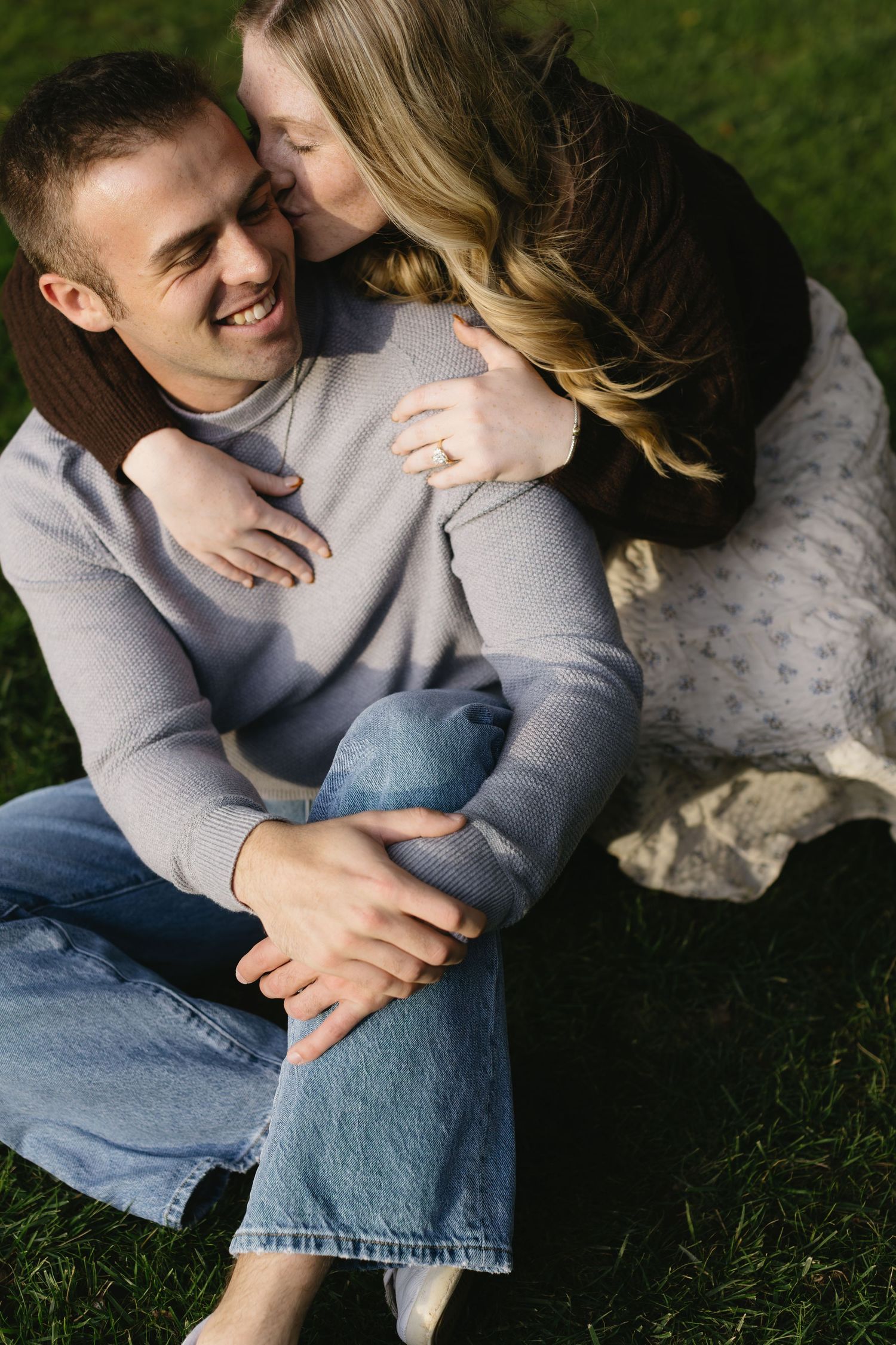 A couple sharing an intimate moment while sitting on grass in a park setting.