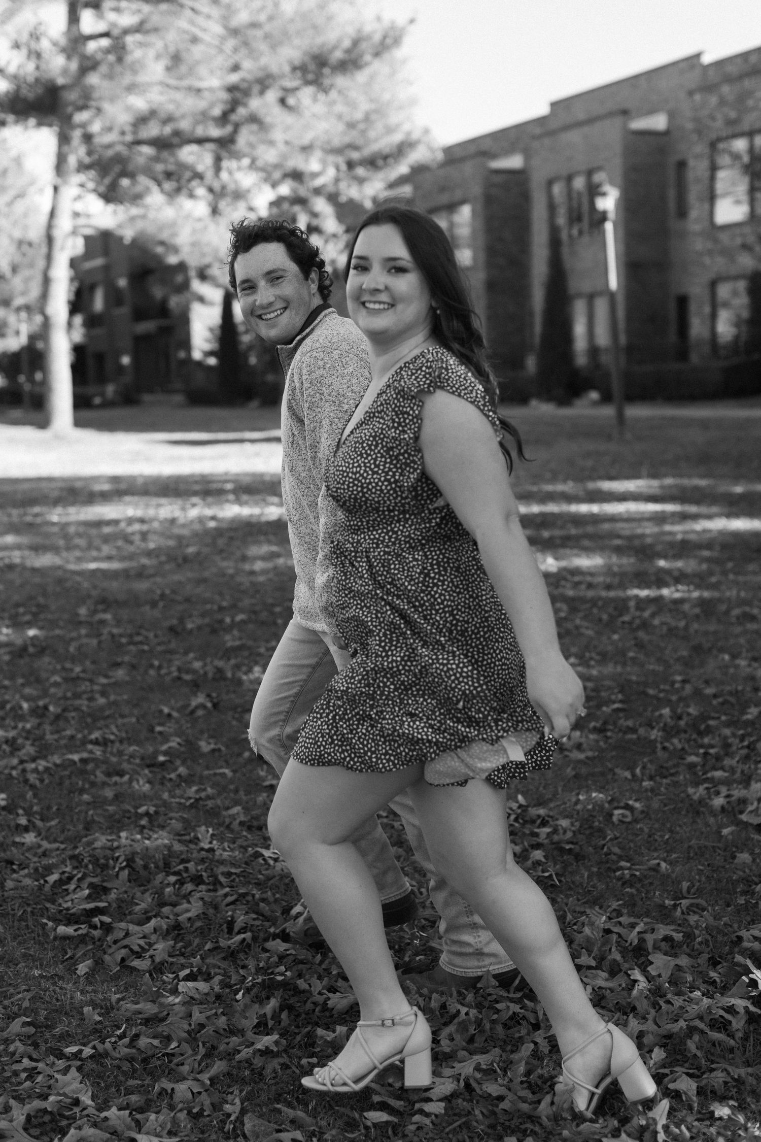 A couple plays and laughs together on fallen autumn leaves in black and white.