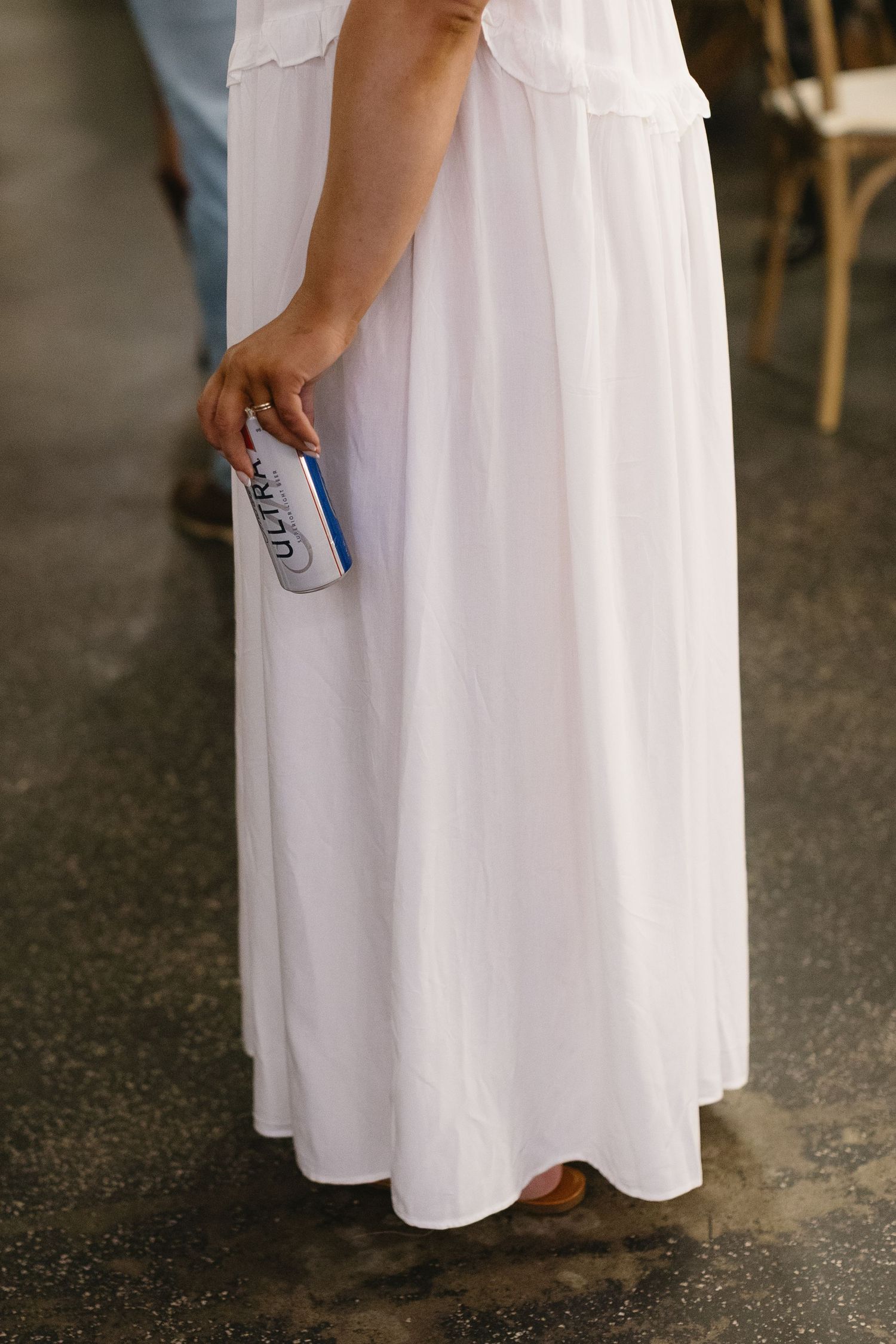 Close-up view of a white dress with a person holding a drink can at a wedding event.