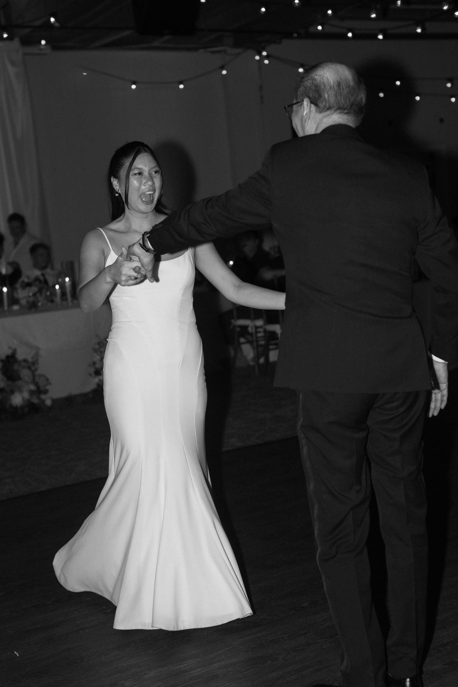Black and white photo of wedding reception dancing with twinkling lights overhead.