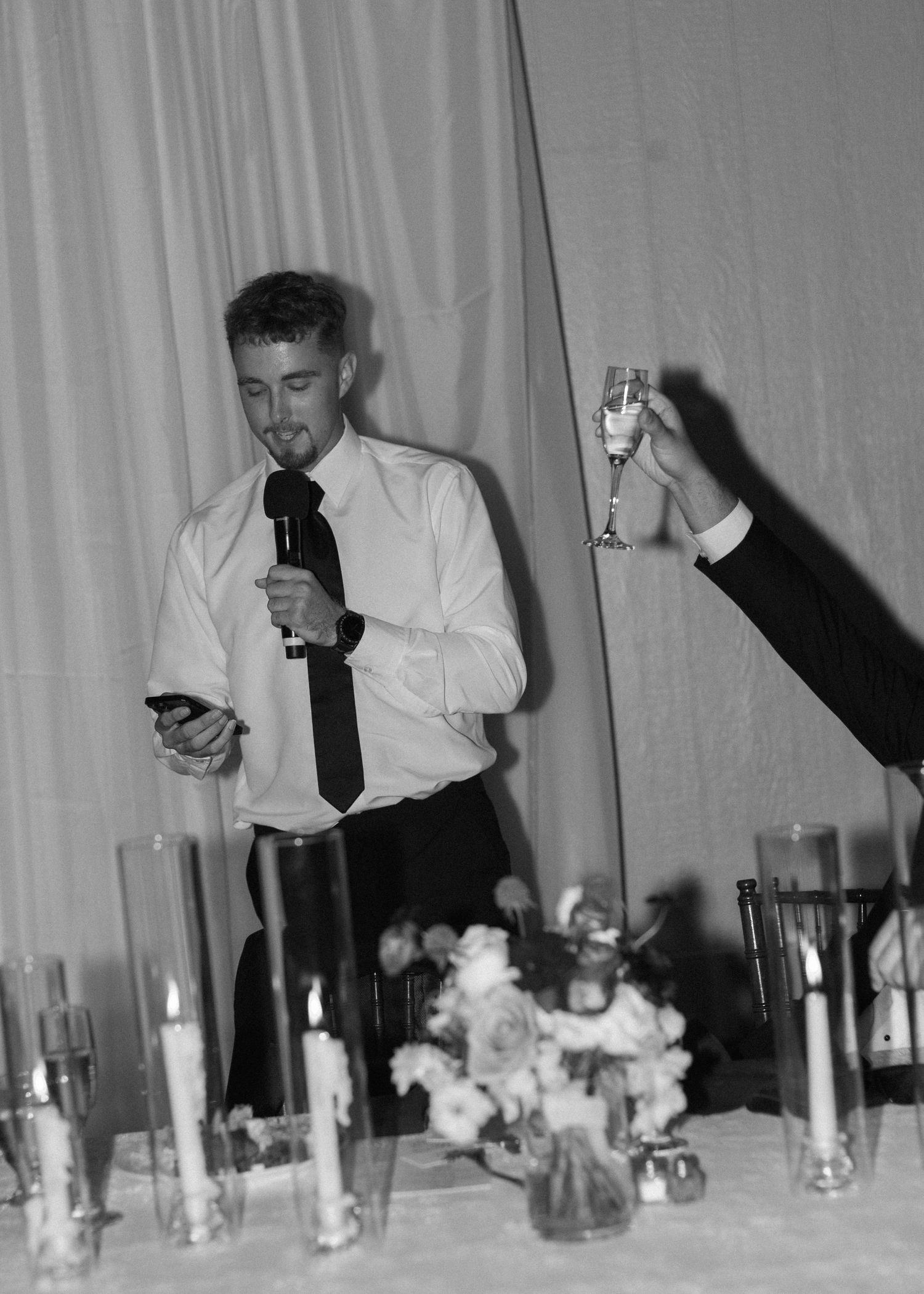 Black and white photo of reception table with candles and floral arrangements.