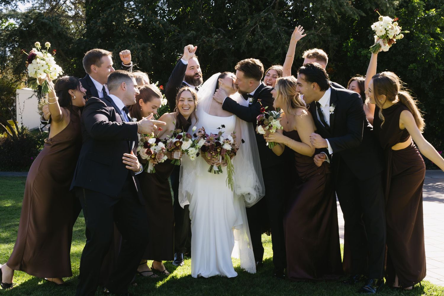 Joyful wedding party celebration photo with people jumping and cheering outdoors.