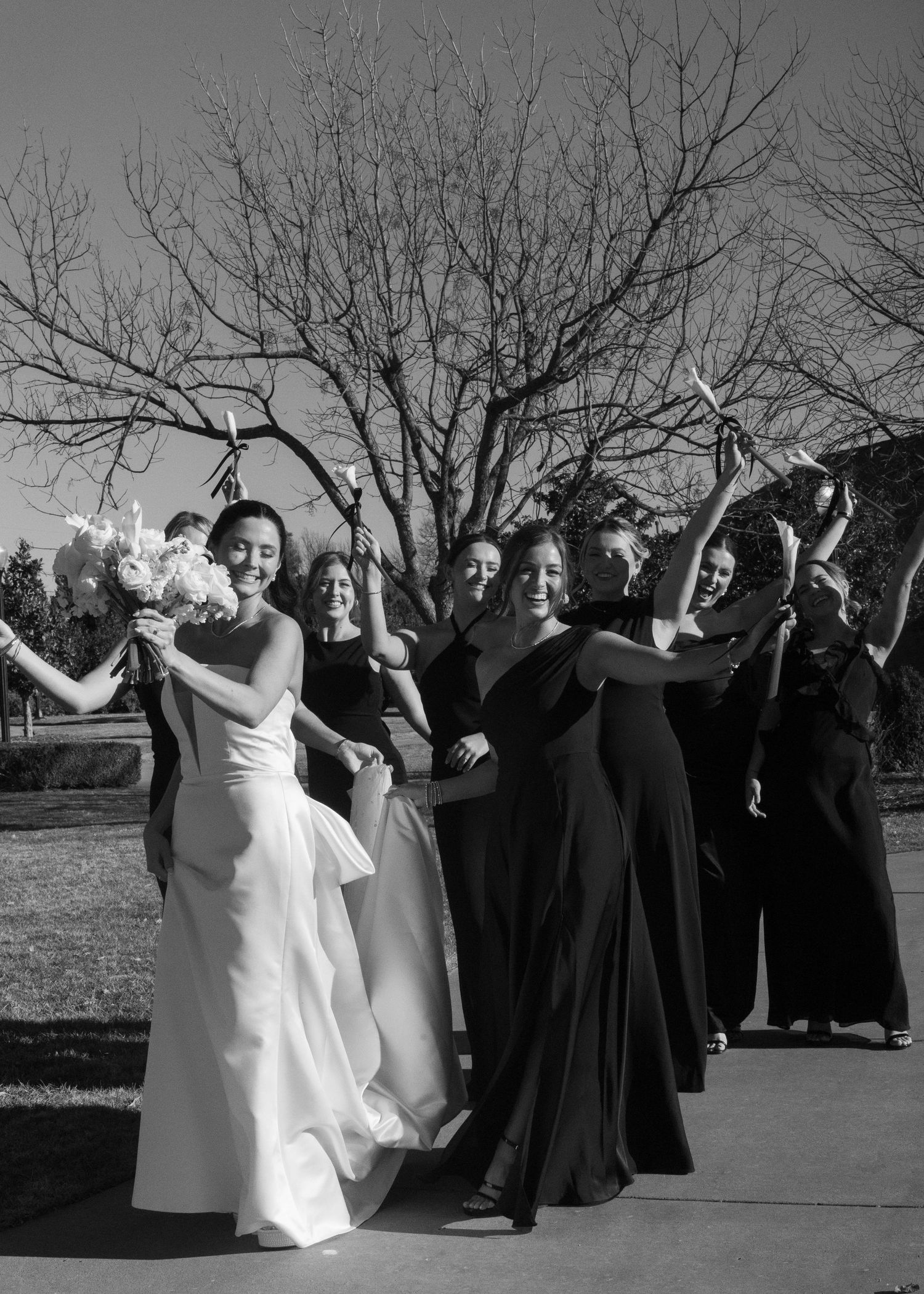 Black and white photo of wedding party celebrating outdoors with raised bouquets.