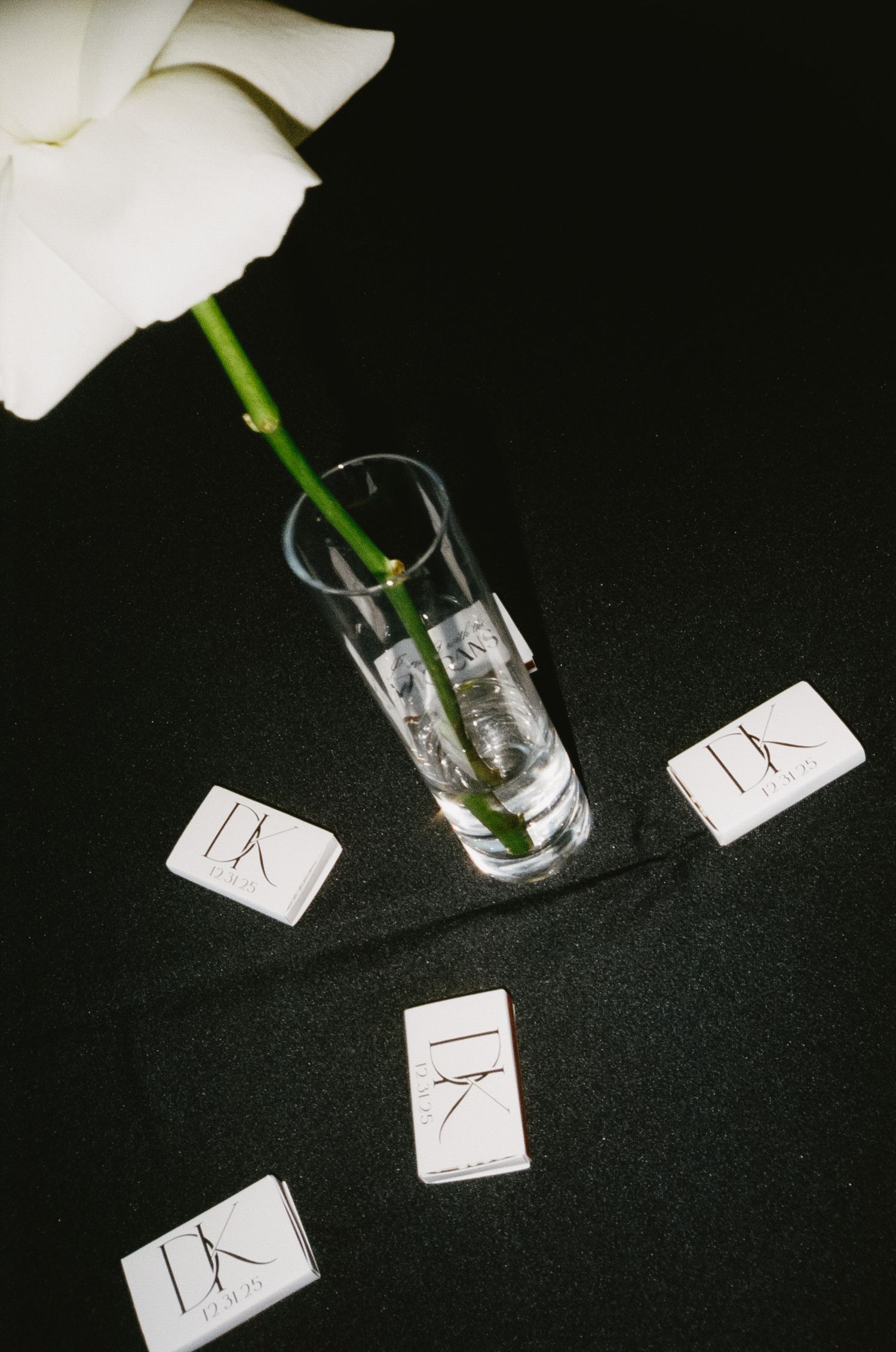 White flowers in clear vases with small table number cards on dark surface.