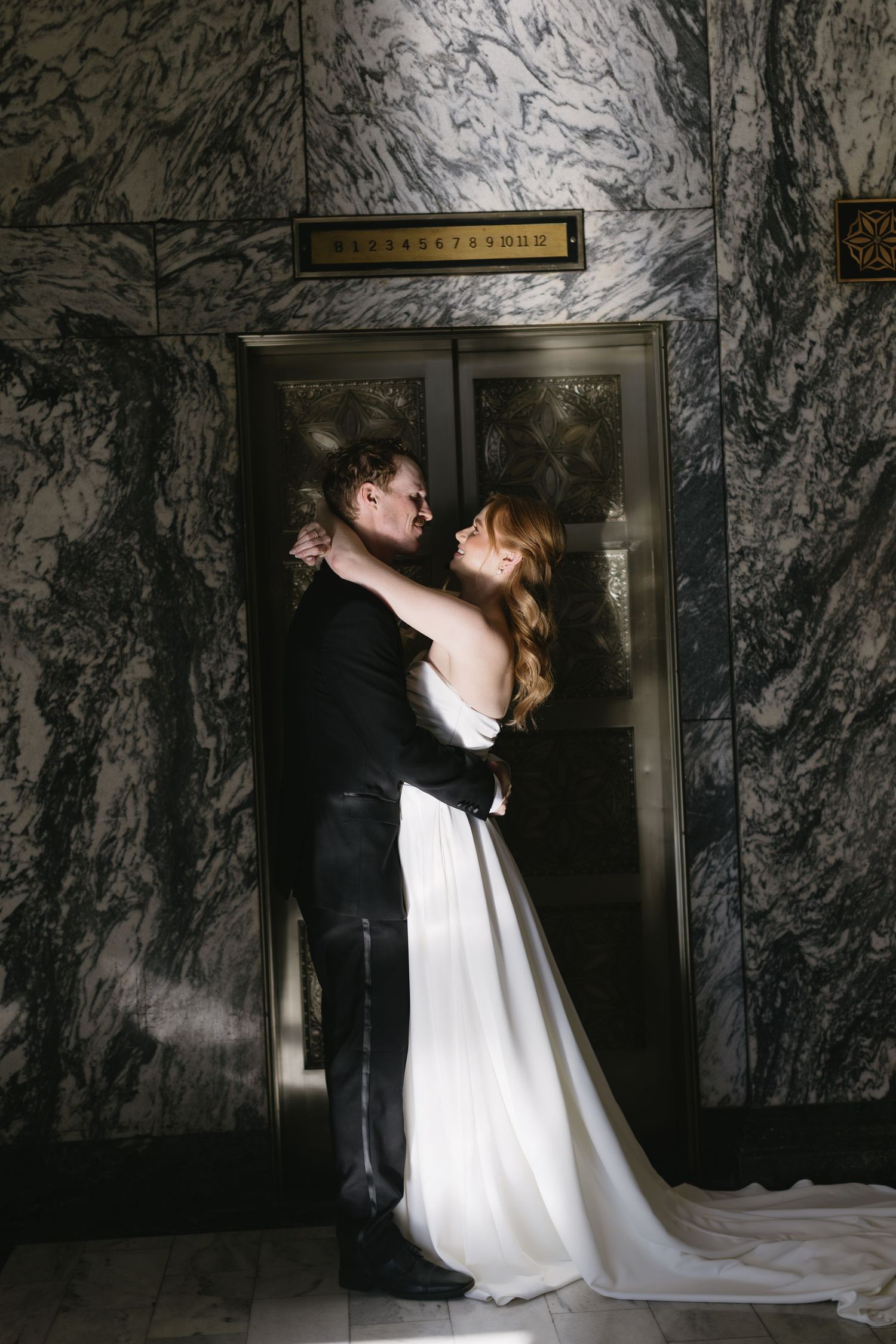 A dramatic wedding photo against marble walls shows a couple in an intimate moment.