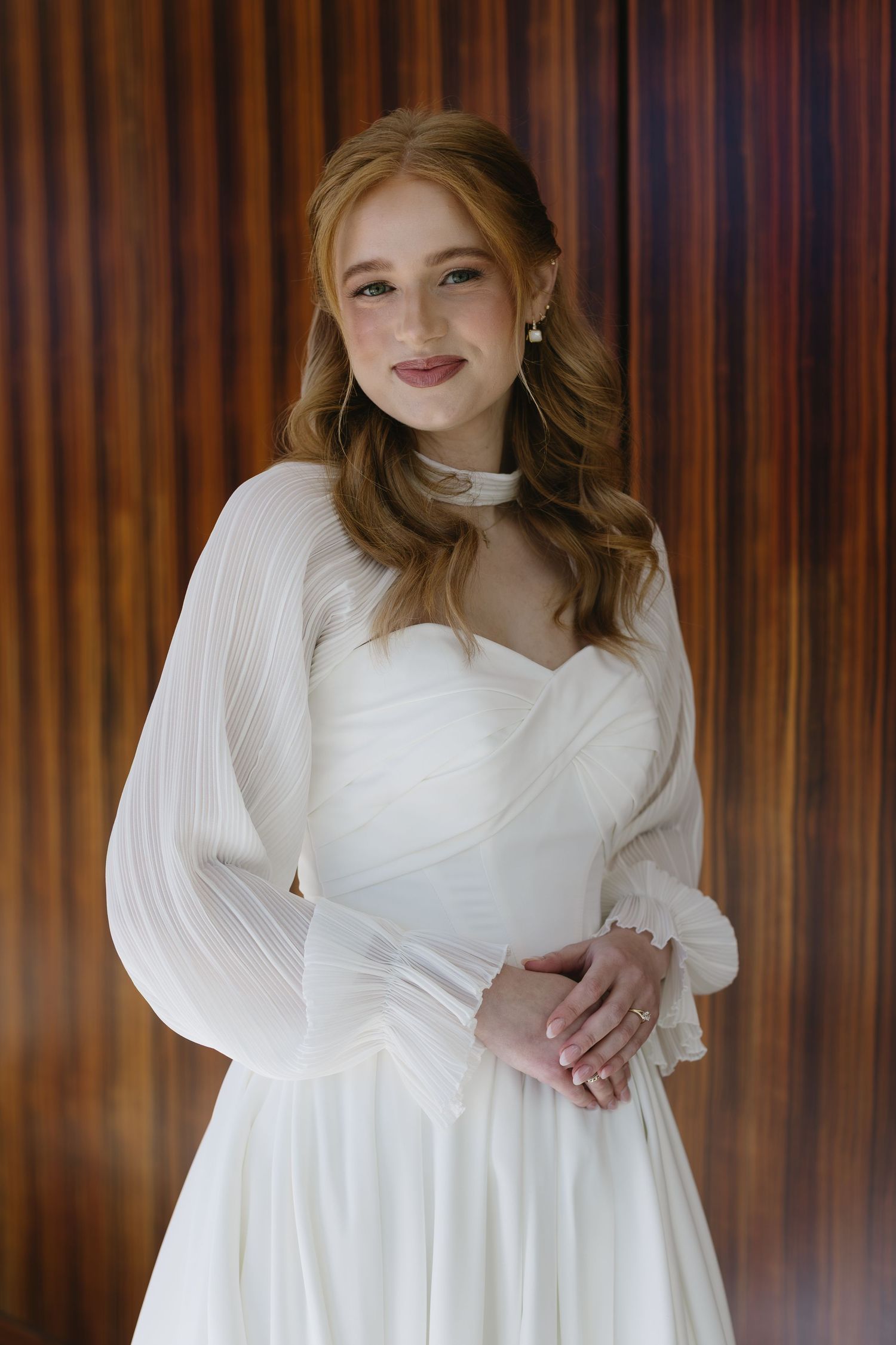 Elegant white wedding dress with sweetheart neckline against wooden paneled background.