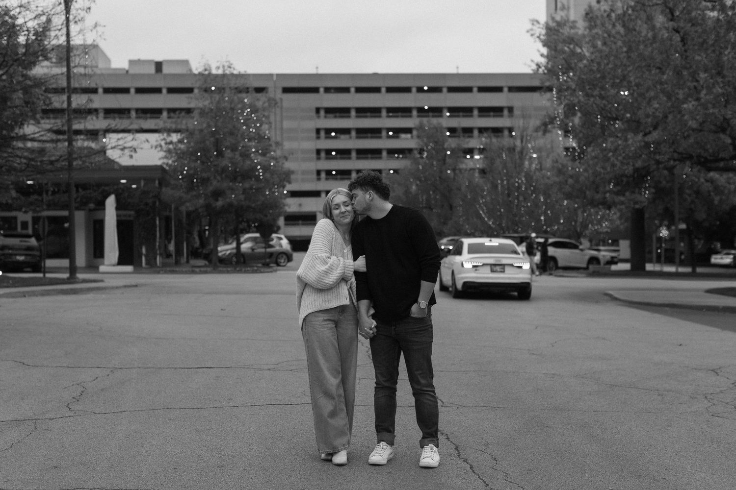 Black and white photo of a couple walking through a parking lot area.