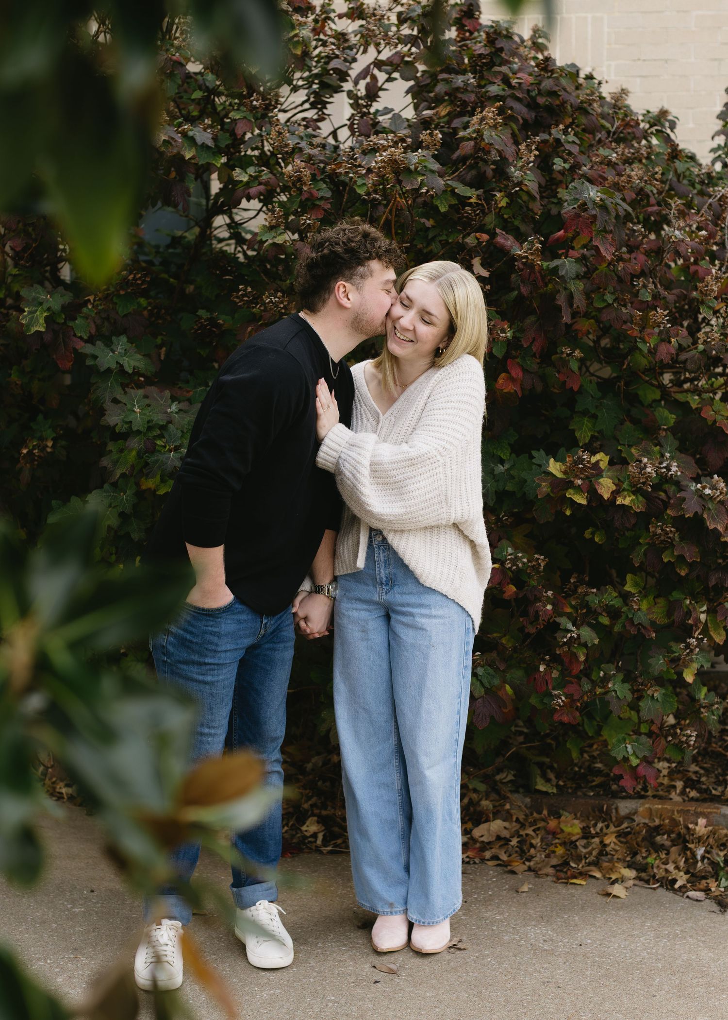 A couple laughs together against a backdrop of red berries and greenery.