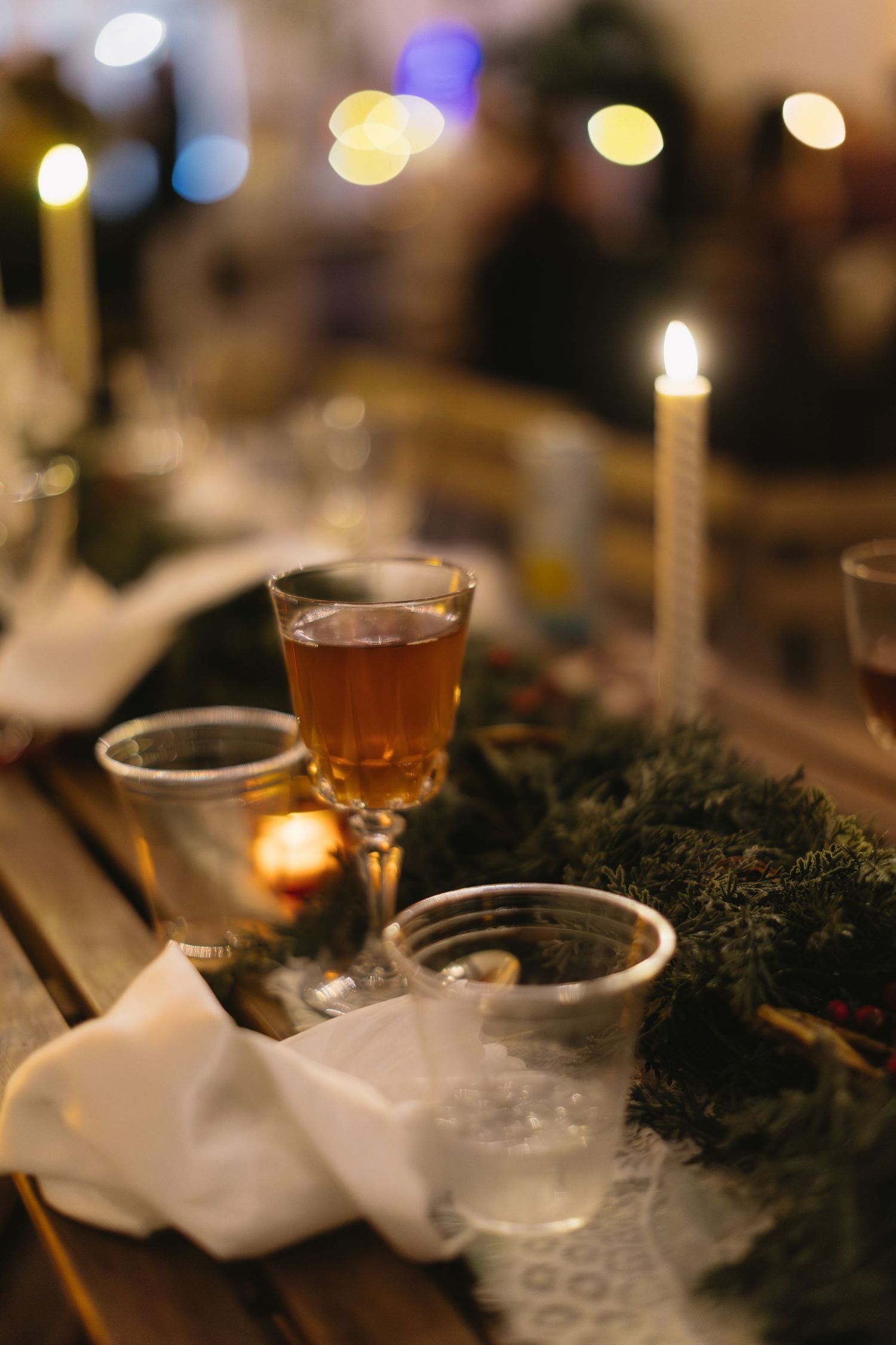 Intimate table setting with candlelight, drinks, and evergreen decorations.