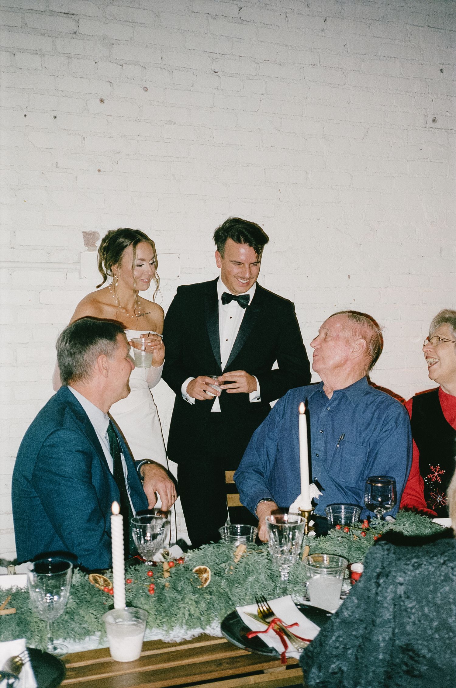 People gathered around a formal dining table with evergreen decorations and glassware.