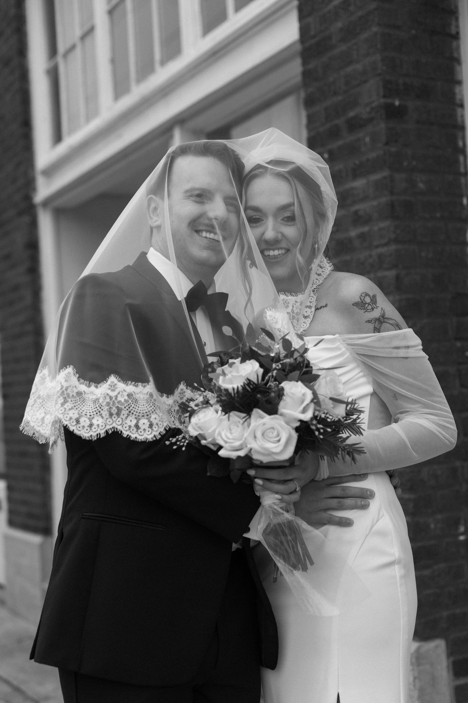 A black and white wedding portrait featuring a couple with a bouquet of roses.