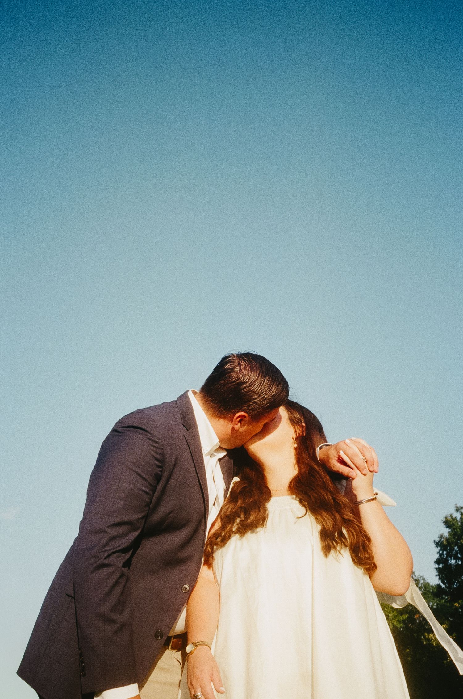 A romantic silhouette against a bright blue sky during a special moment.