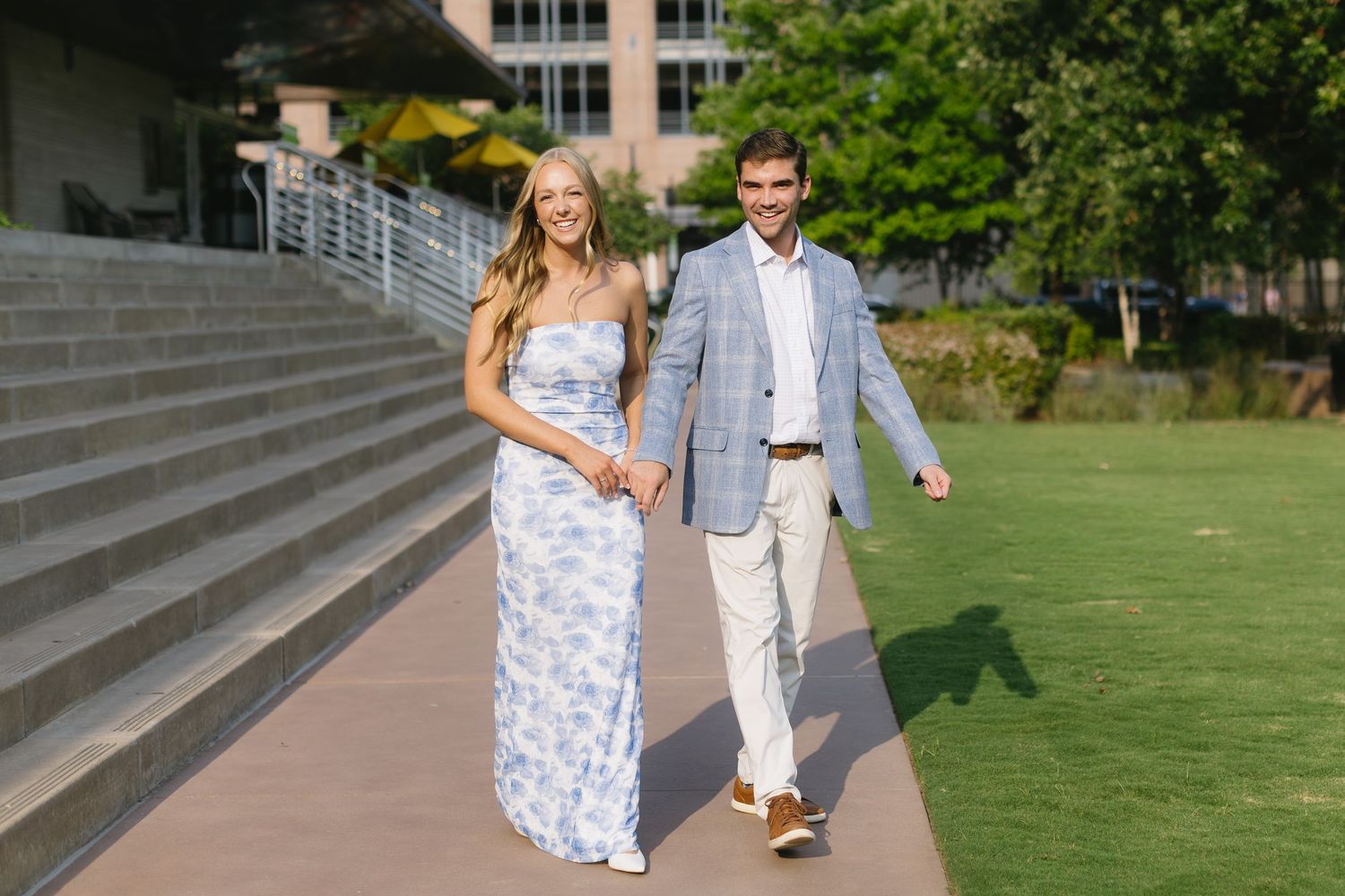 A couple walks together along concrete steps and pathways during a sunny day in a park-like setting.