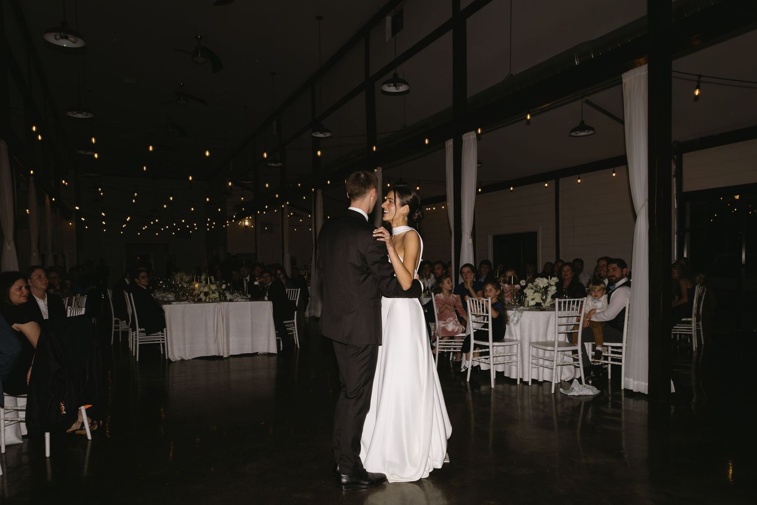 Romantic dance floor scene at wedding reception with string lights overhead.