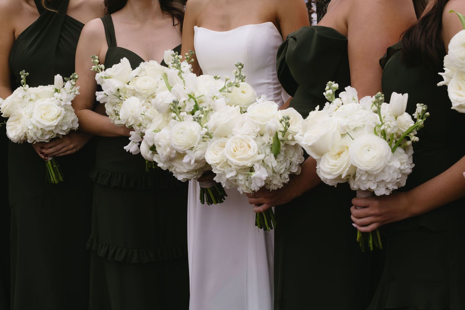 Wedding party holding white floral bouquets against dark attire.
