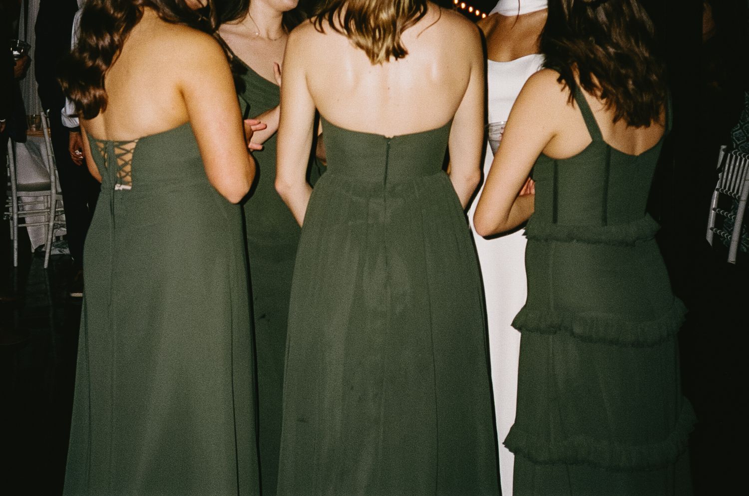 Back view of bridesmaids wearing dark green dresses at a wedding celebration.