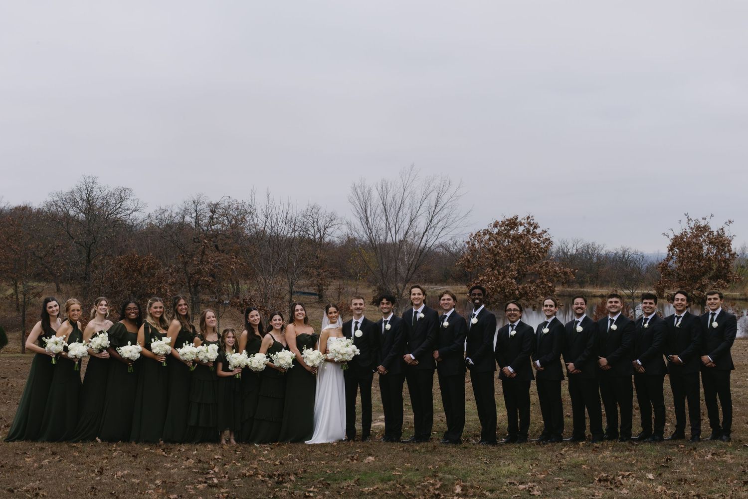 Wedding party lined up outdoors against an autumn landscape backdrop.