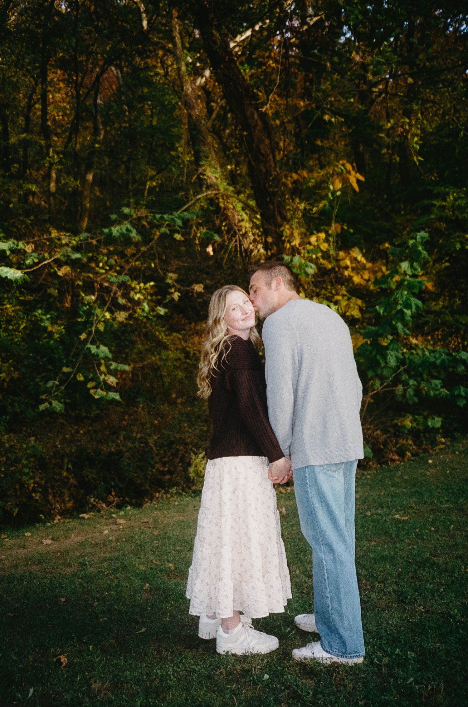 A couple shares a romantic moment in an autumn forest setting with golden leaves and natural lighting.