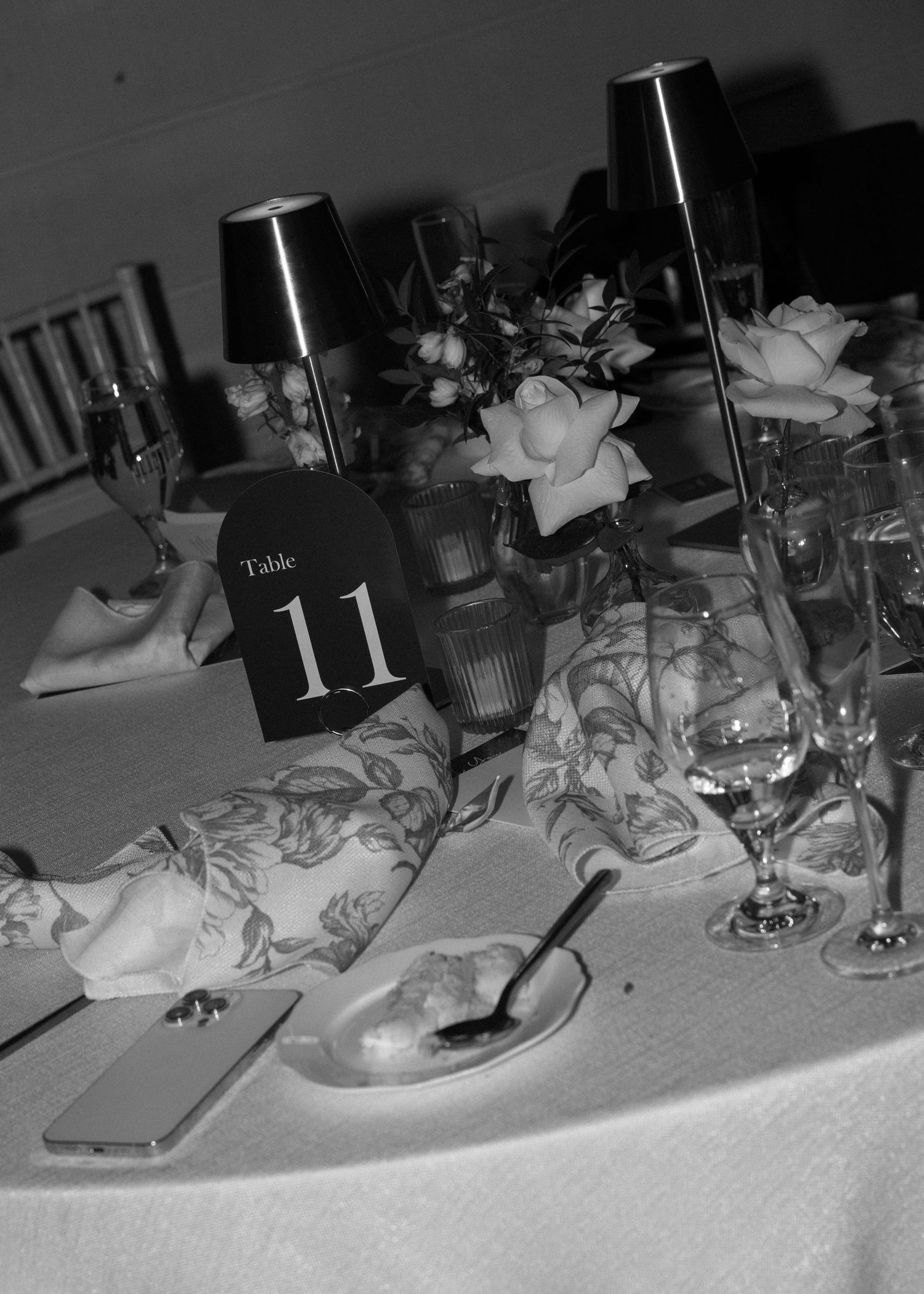 Wedding reception table settings with glassware and decorative elements in dim lighting.