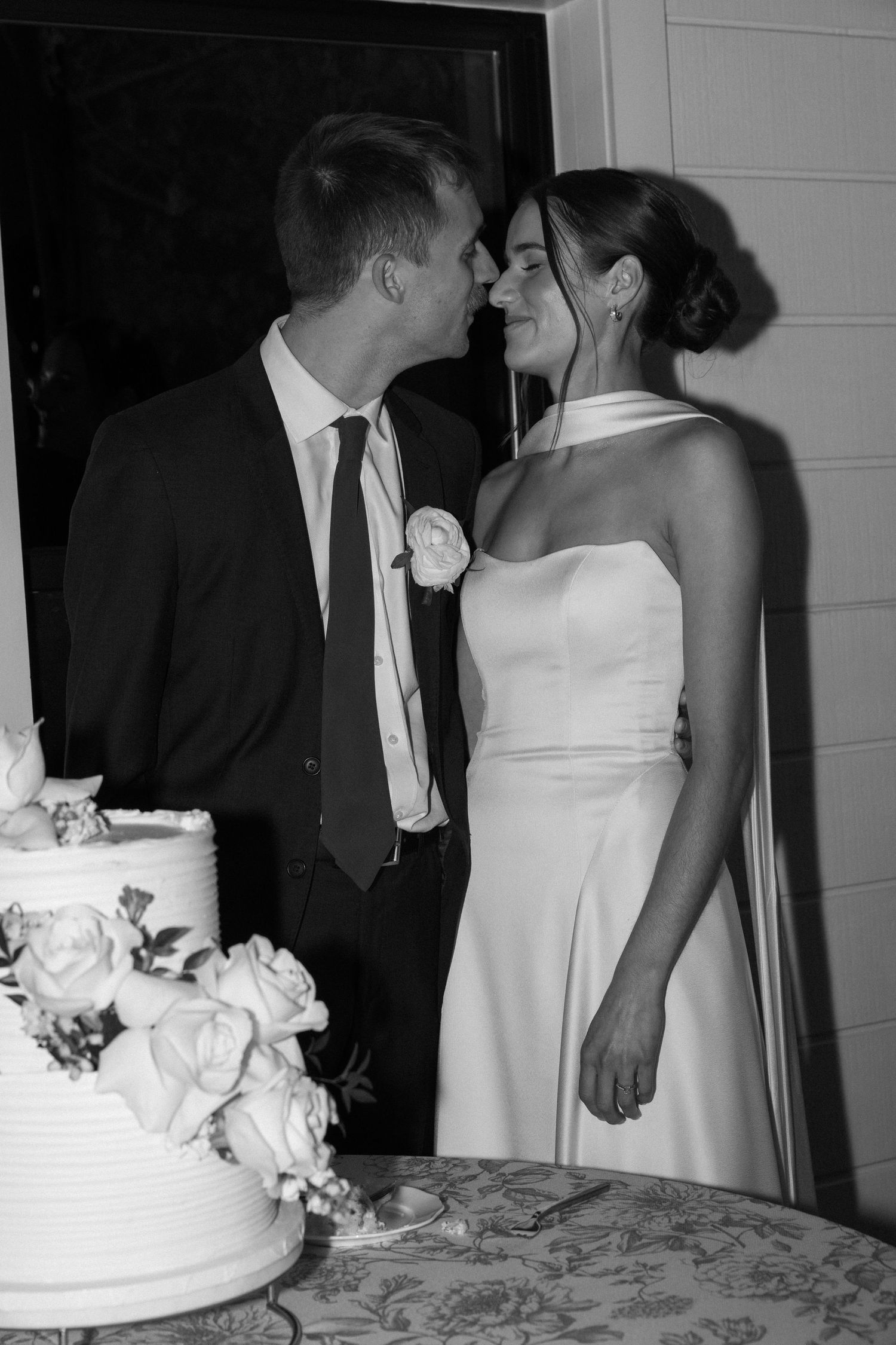 Wedding couple in formal attire standing near their white wedding cake at the reception.