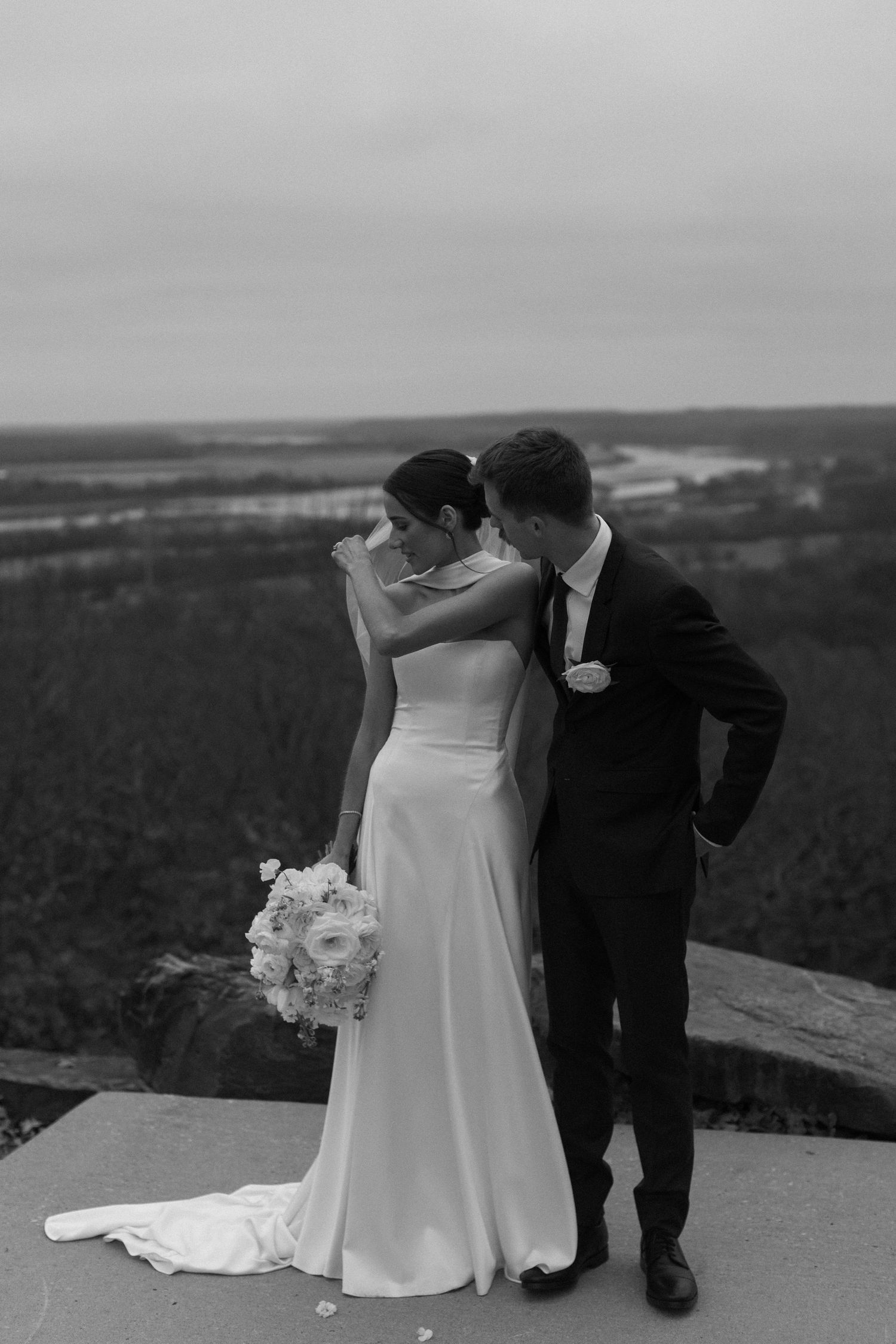 Dramatic wedding portrait on mountain overlook with sweeping valley views in black and white.
