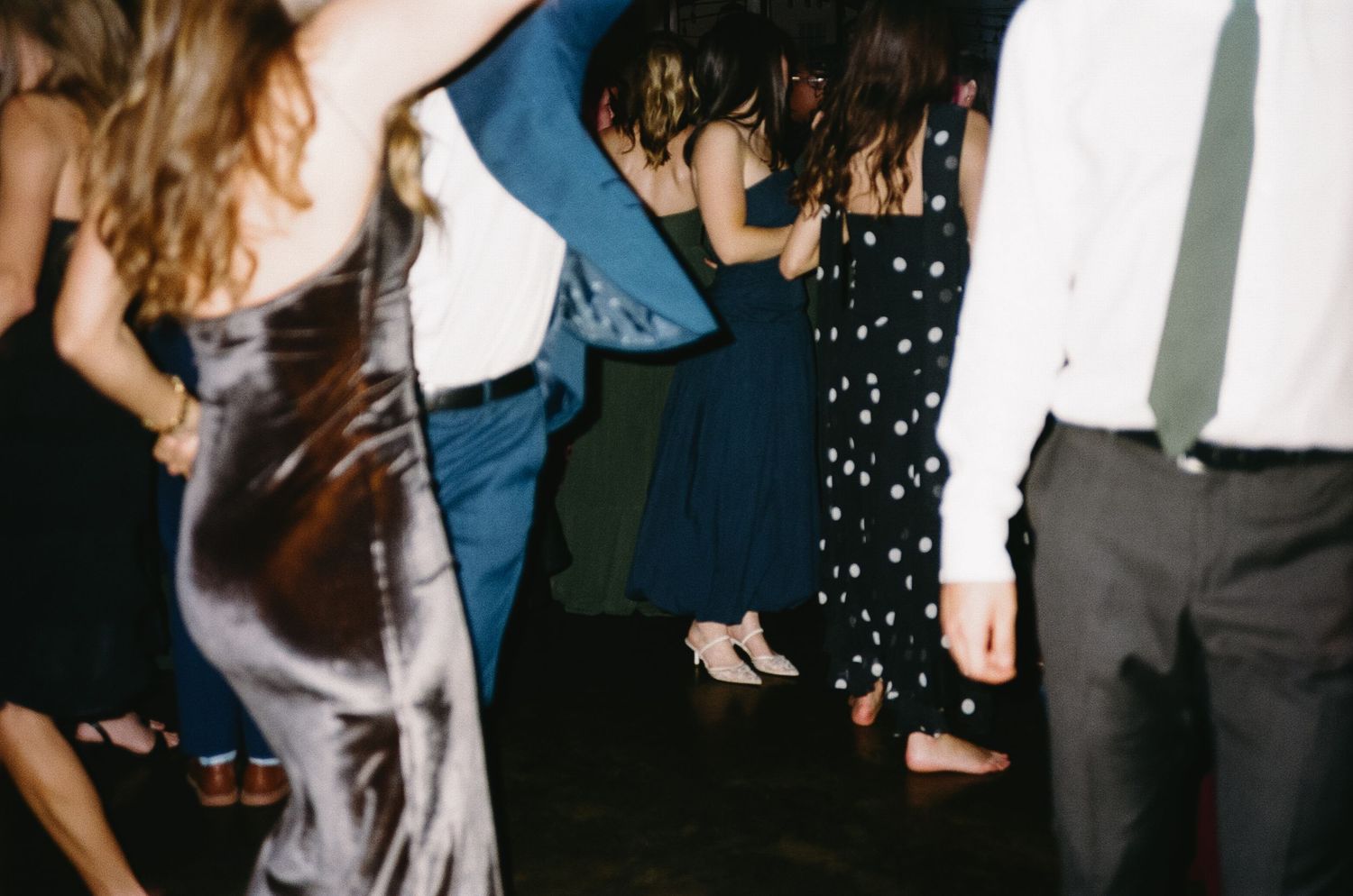 Wedding guests dancing in formal attire on a dark dance floor with festive lighting.