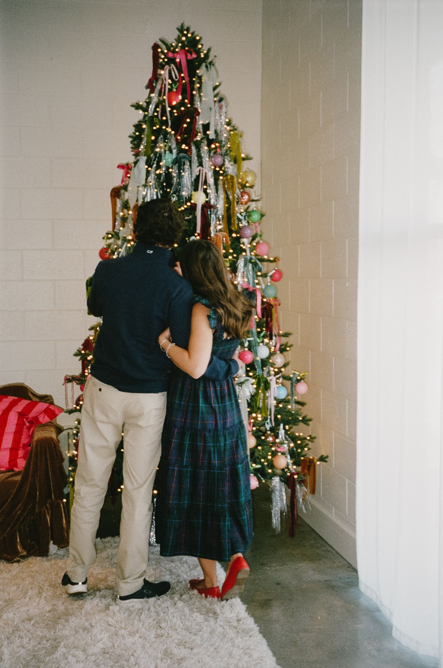 Multiple shots of people standing beside a decorated Christmas tree in a room with white walls.