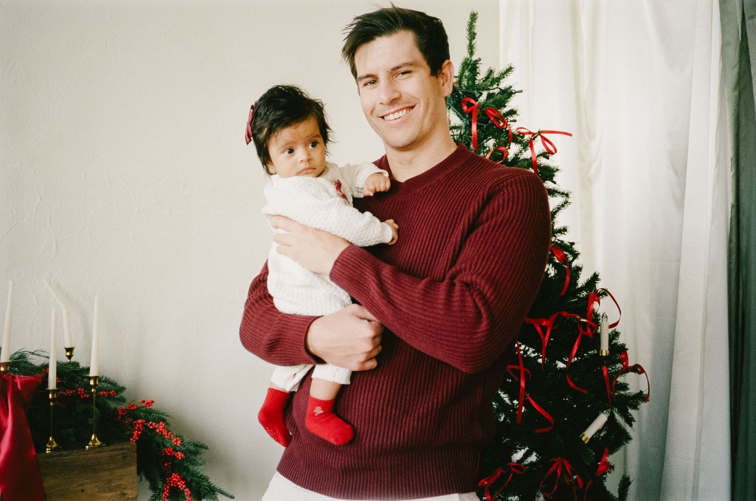 Parent and child wearing matching burgundy sweaters pose together by a decorated Christmas tree in four similar photos.
