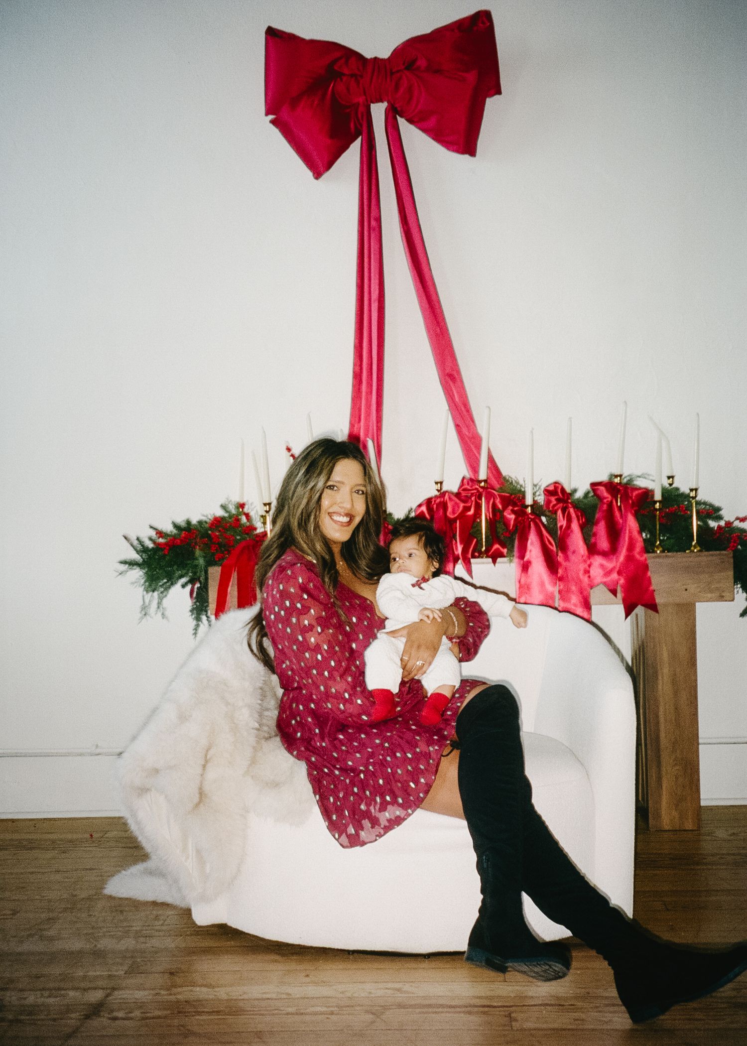 A festive holiday photo shoot setup with red bows and white decorations against a brick wall.