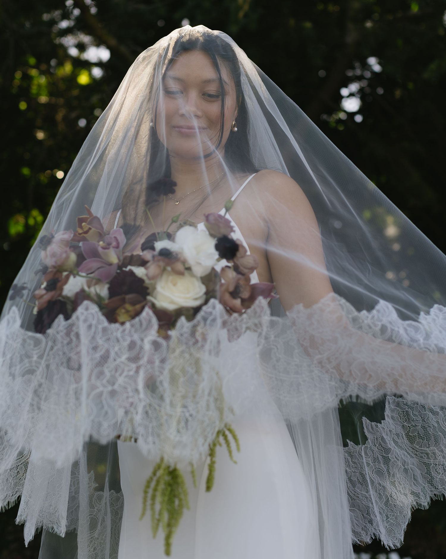 Delicate lace veil with floral details flows elegantly in an outdoor wedding setting.