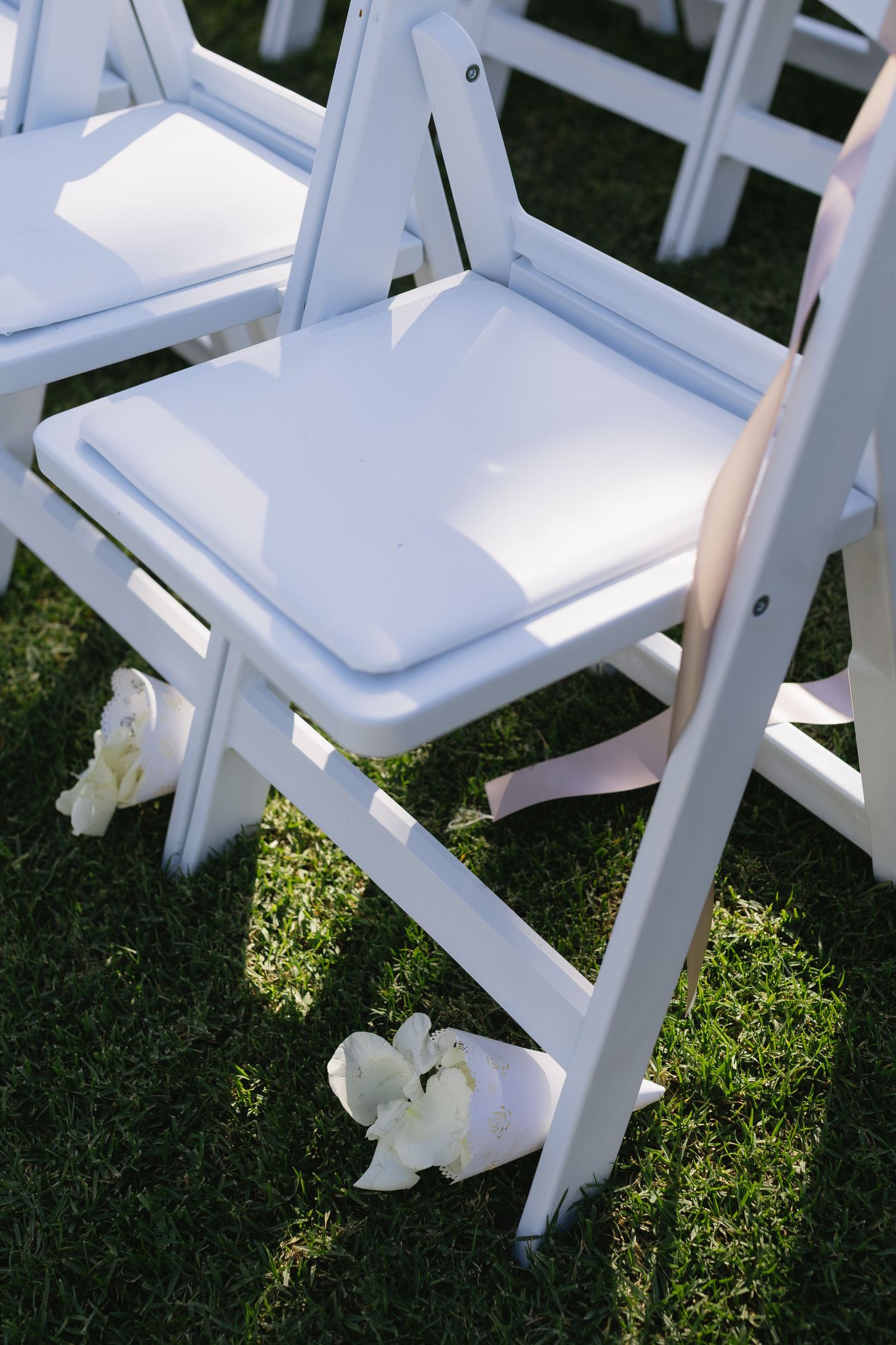 White folding chairs arranged on grass for an outdoor wedding ceremony.