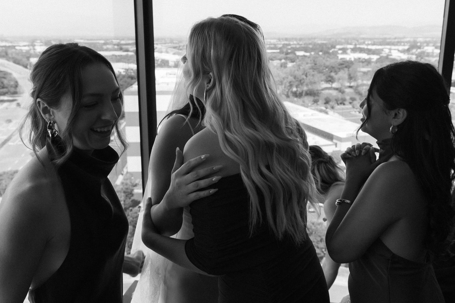 Silhouettes gather by large windows overlooking a cityscape view.