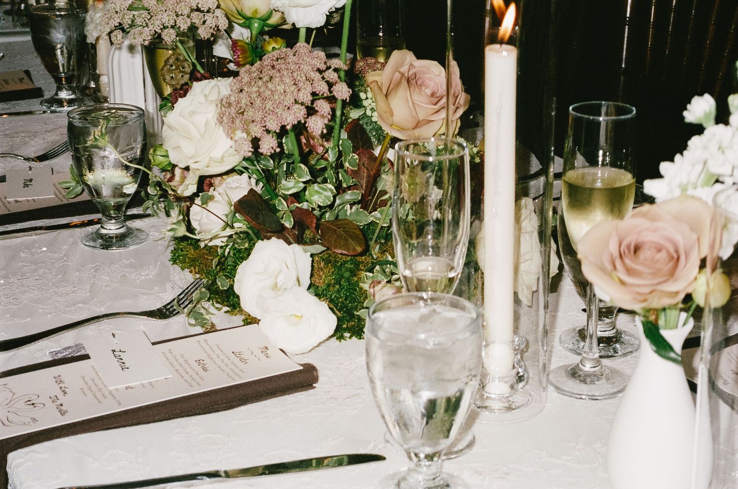 Elegant floral centerpieces with pink roses and greenery decorate wedding reception tables.