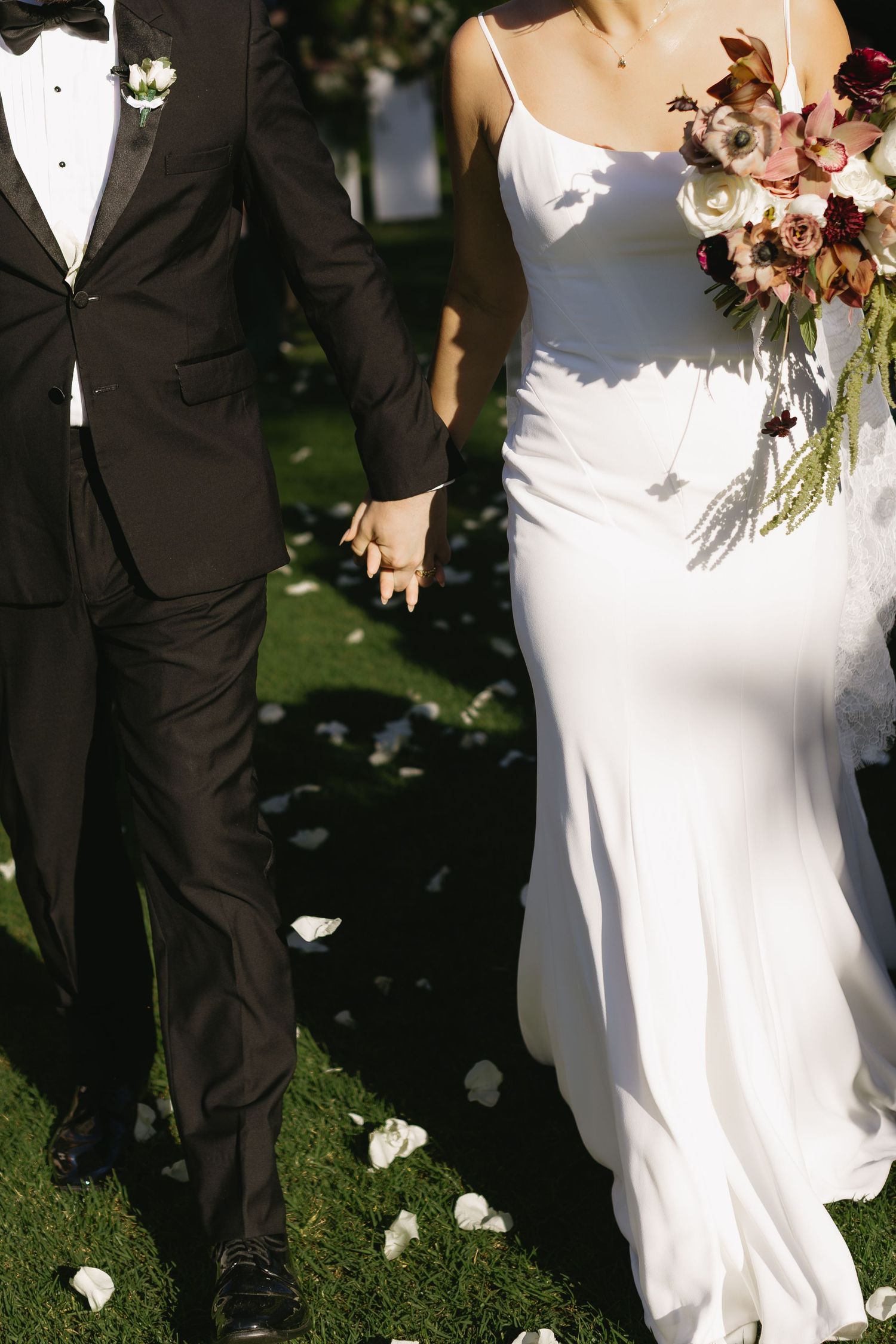 Elegant wedding ceremony details with bride in white gown and groom in tuxedo on sunny lawn.
