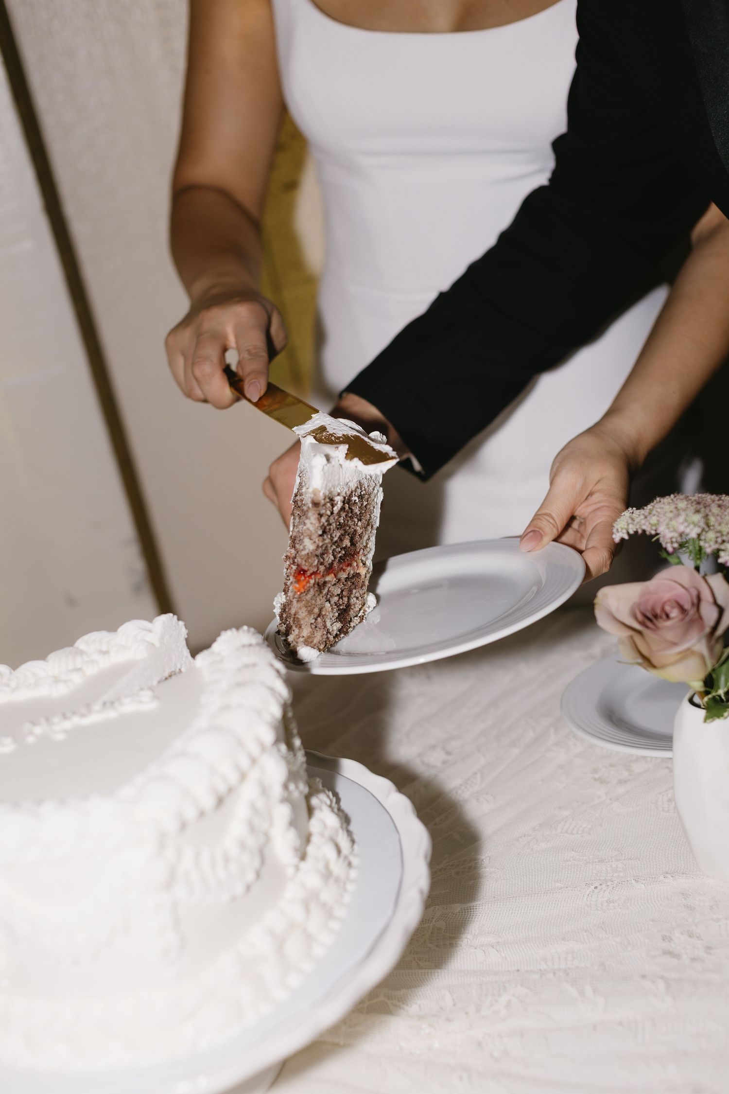 Close-up shots of hands cutting and serving traditional white wedding cake.