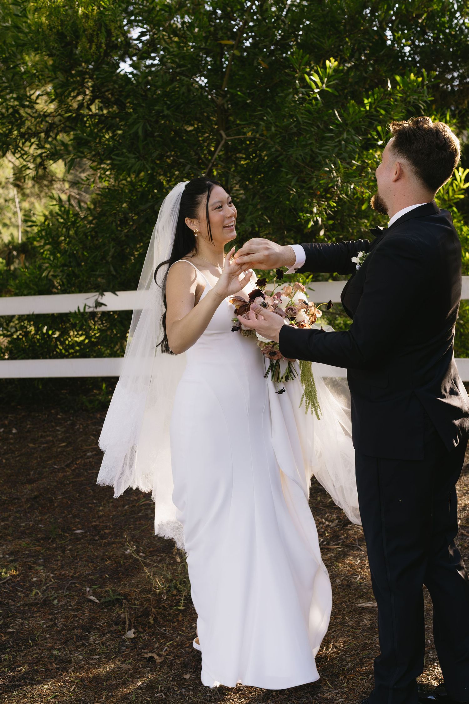 A couple shares a playful dance moment outdoors with flowing white dress and veil movement.