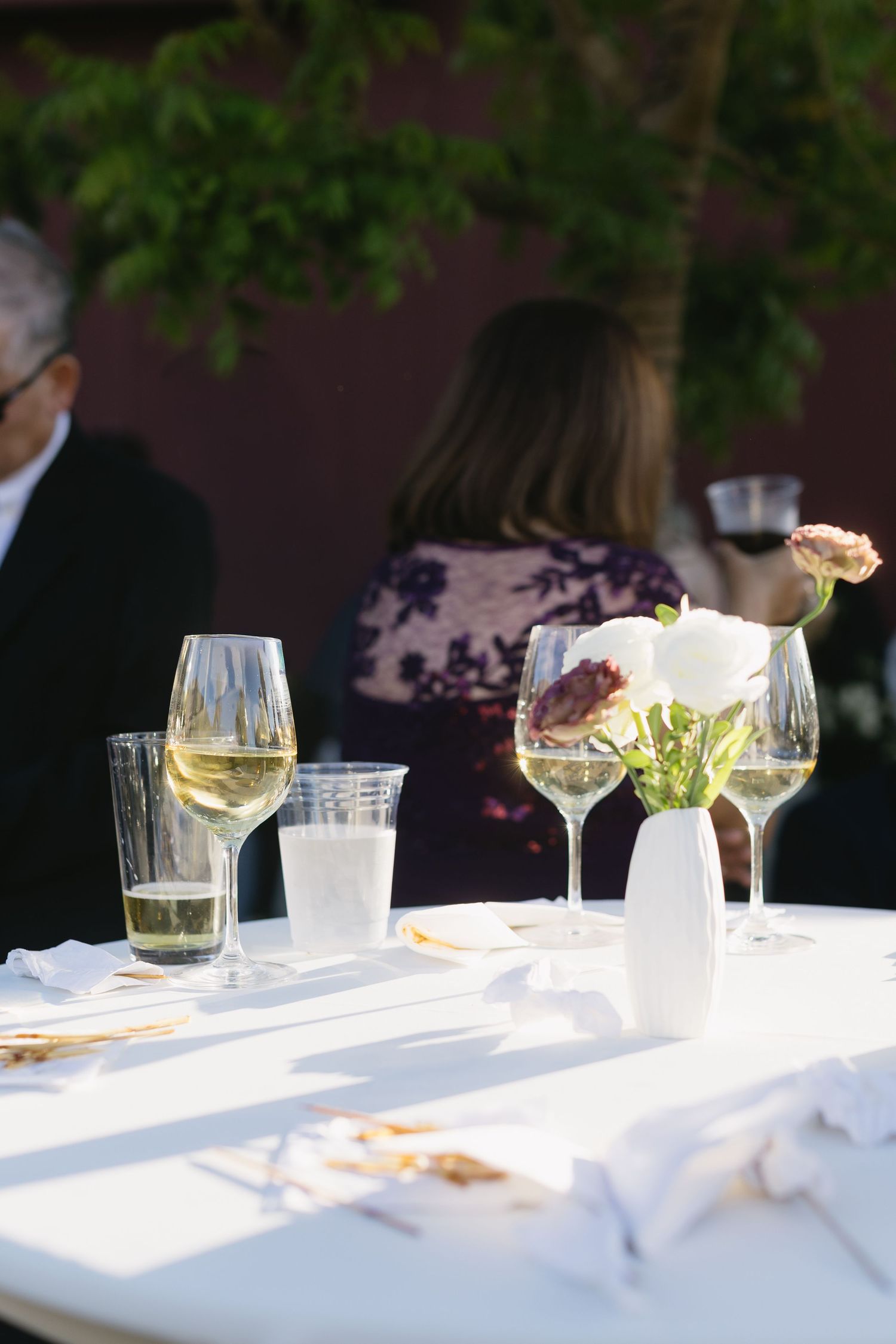 Elegant table setting with wine glasses and white linens in outdoor garden lighting.