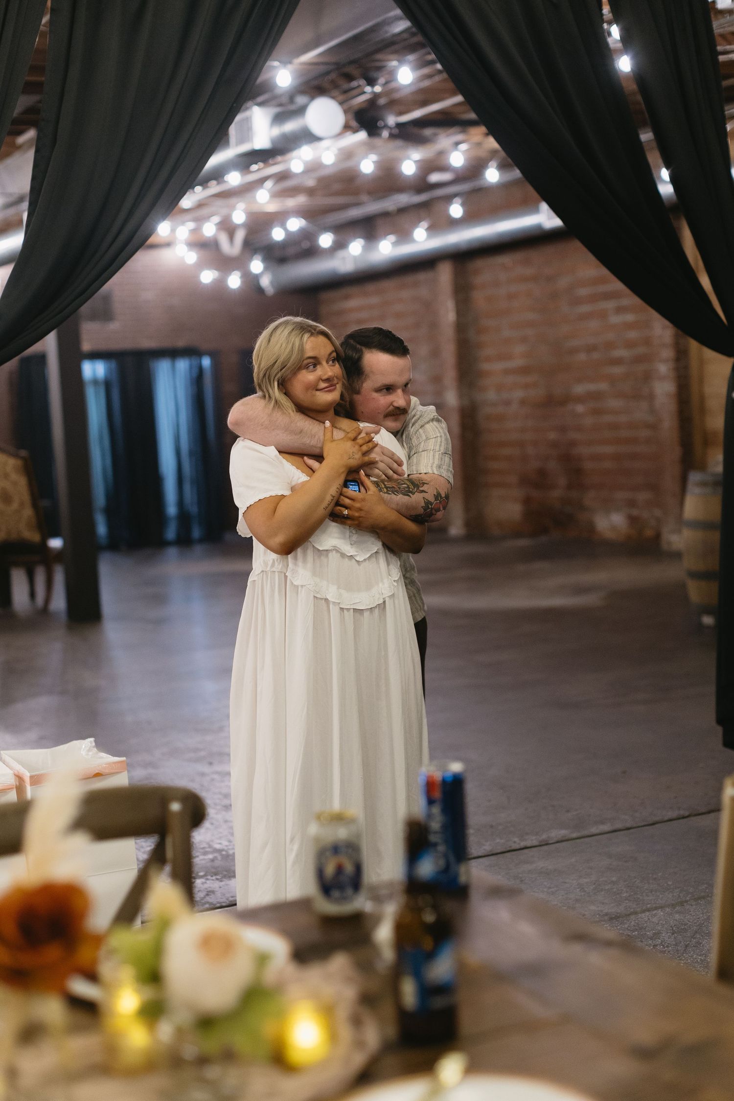 Couple sharing an intimate moment under draped curtains with twinkle lights at a rustic venue.