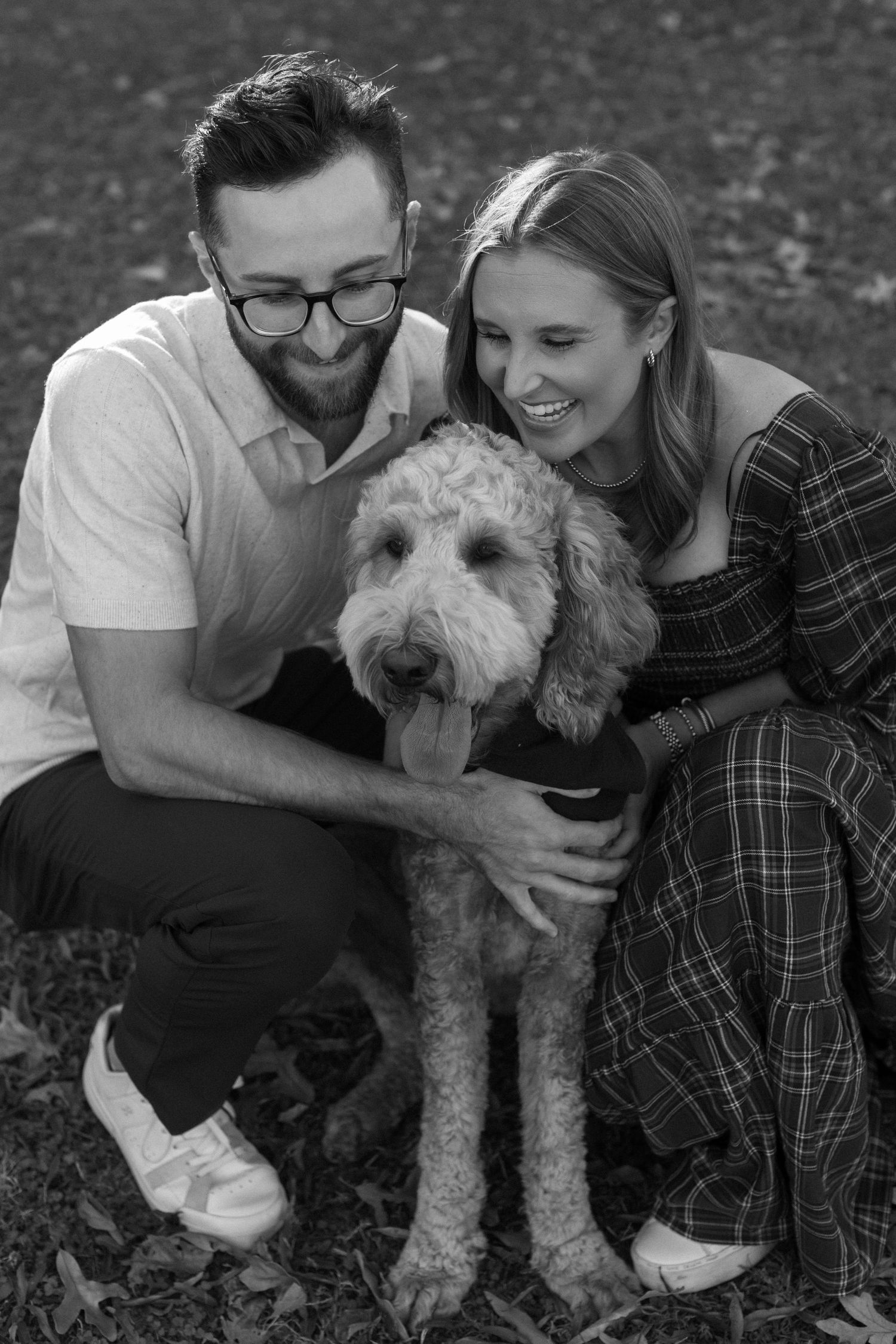 A couple and their fluffy white dog pose together outdoors in a series of casual black and white photos.