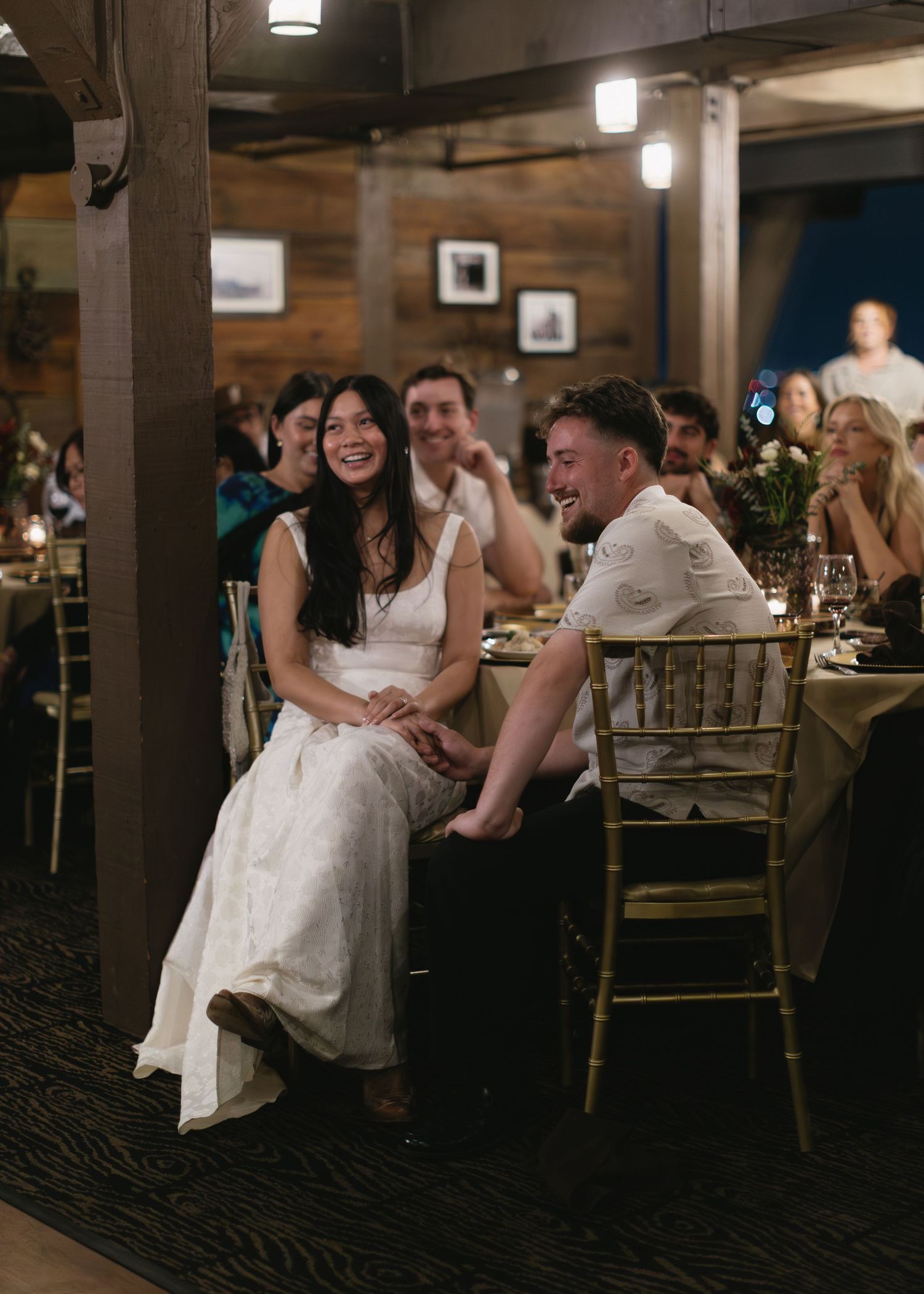 Wedding reception scene in a dimly lit venue with guests seated at decorated tables.