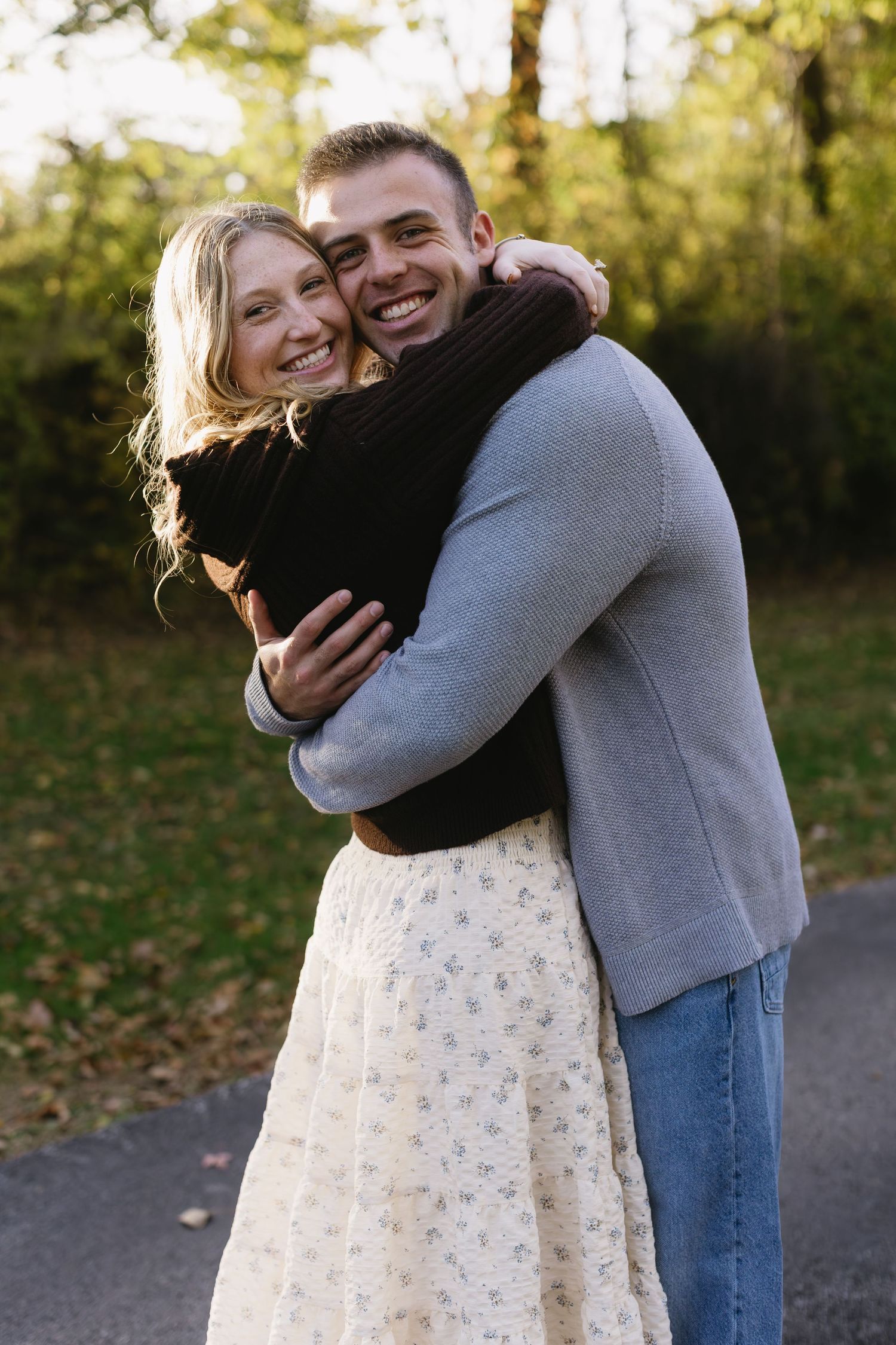 Couple sharing tender moments in autumn setting with golden sunlight filtering through trees.