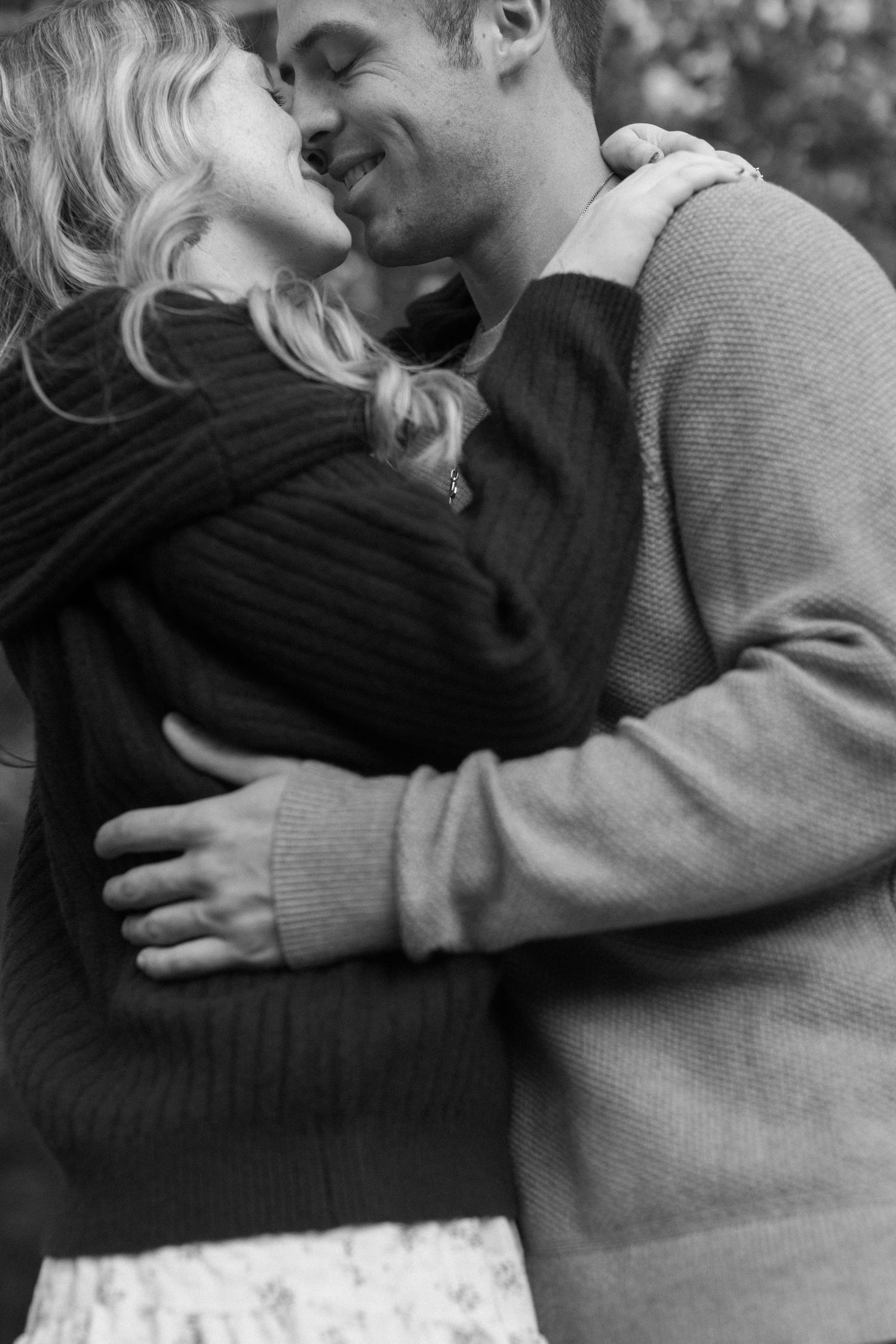 A black and white portrait of a couple sharing an intimate embrace outdoors.
