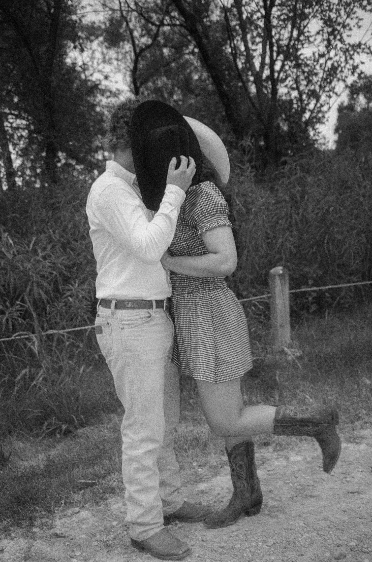 A romantic black and white photograph of a couple embracing on a dirt path, with trees in the background.