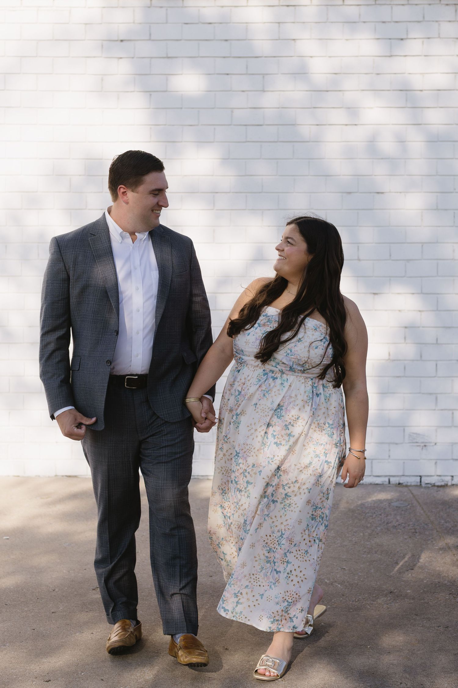 Casual walking poses of a couple in formal wear against a white wall.