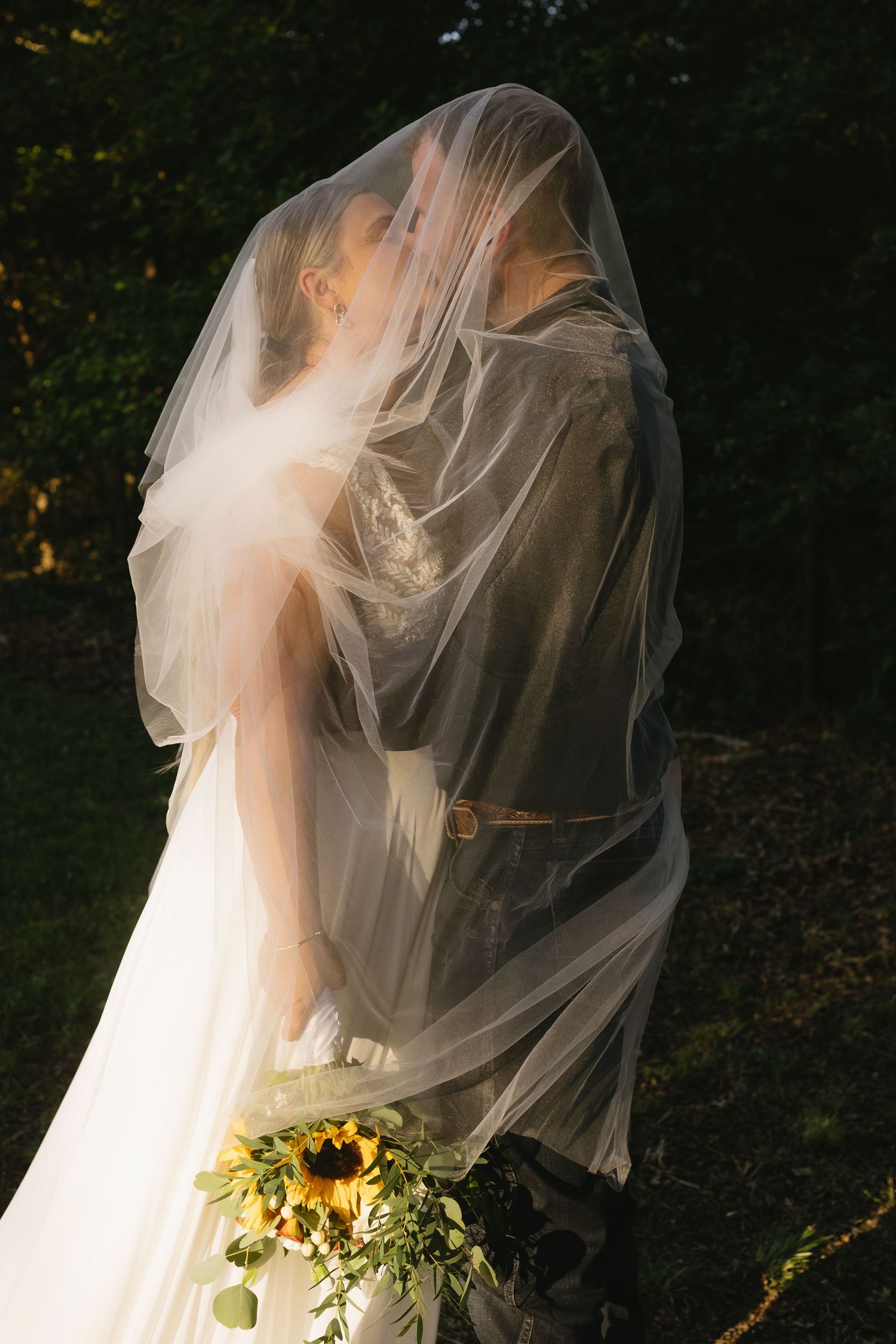 Ethereal sunlit portrait of a bride with flowing veil and sunflower bouquet.