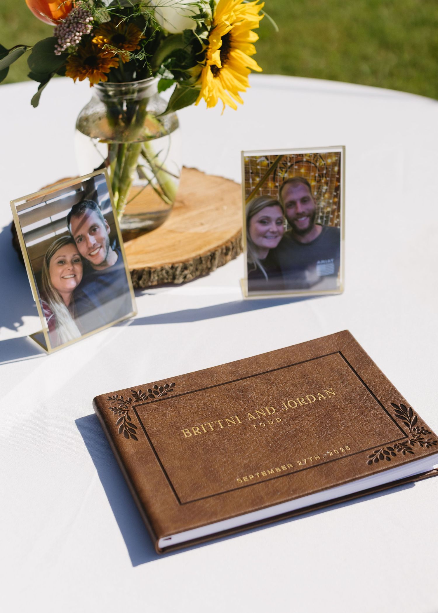 Wooden wedding guest book with sunflowers and photos displayed on a white tablecloth.