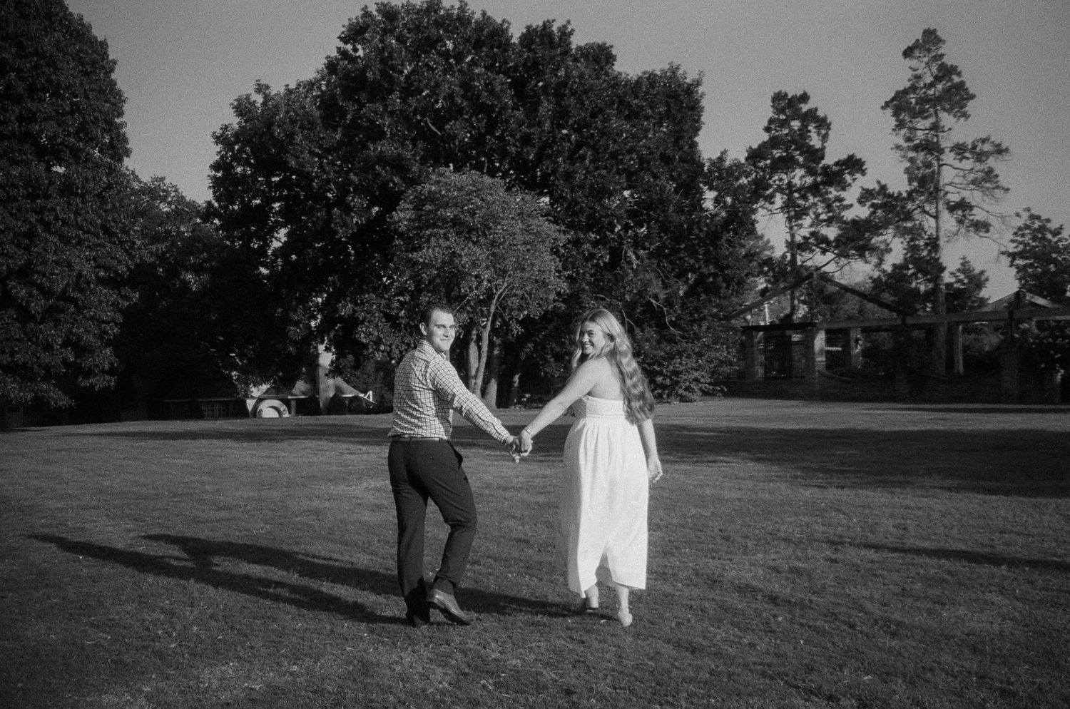 Black and white wedding photos show couple walking through scenic outdoor venue with trees and grassy landscape.