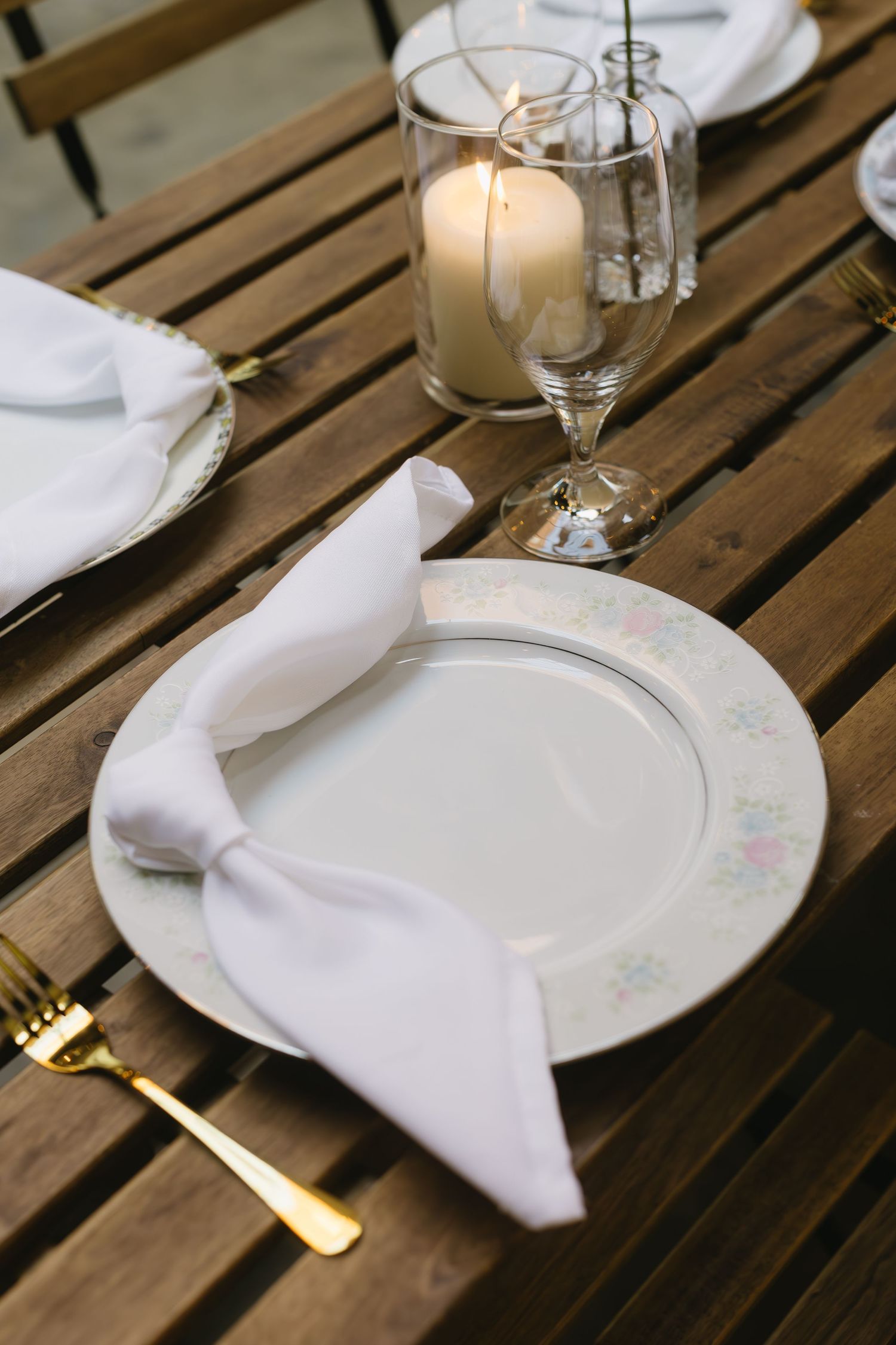 Elegant table setting with white plates and napkins on wooden slat surface.
