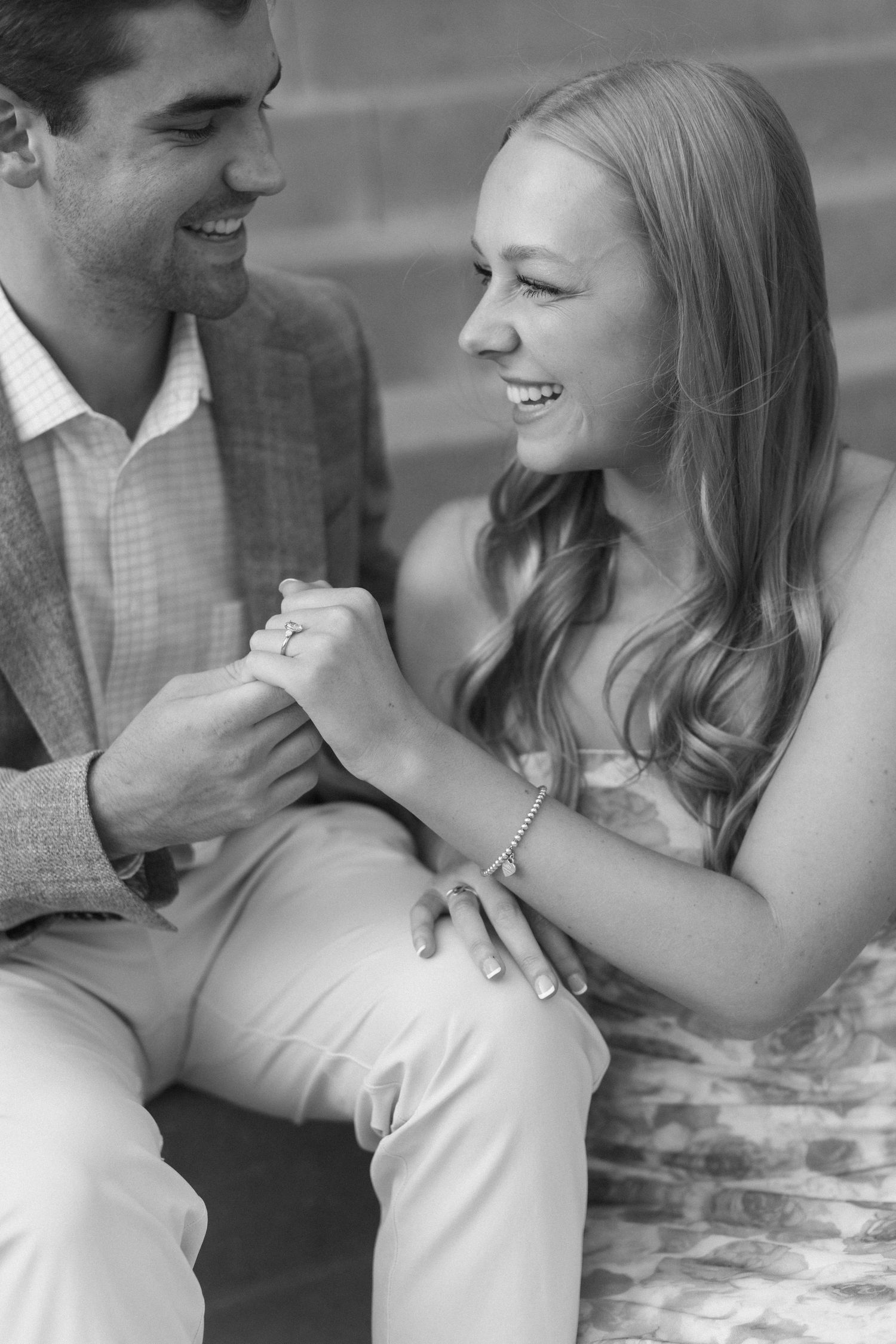 A romantic black and white photo of a couple laughing while sitting outdoors.